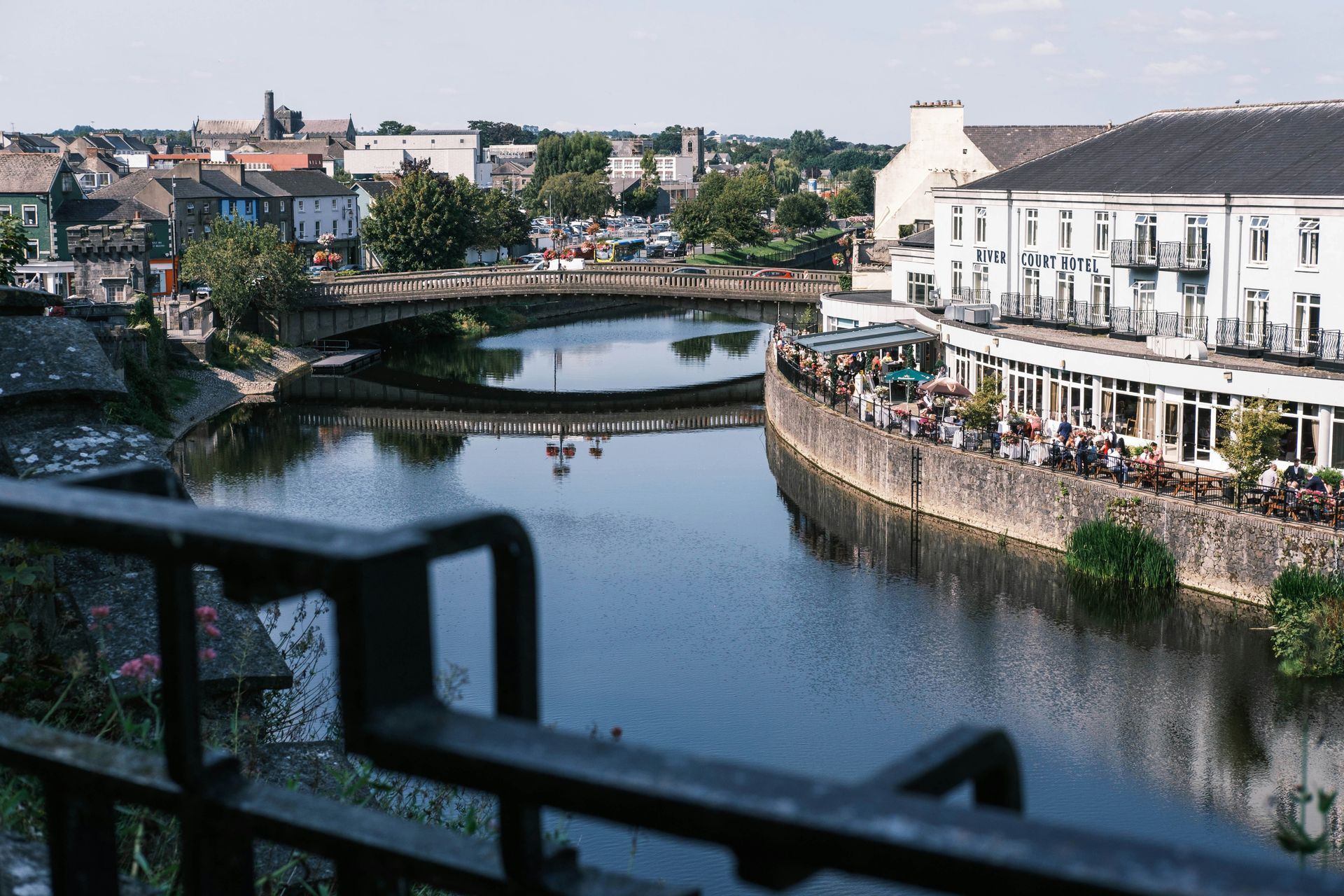 River flowing through a town with a bridge and a white building with outdoor seating in Kilkenny, Ireland.