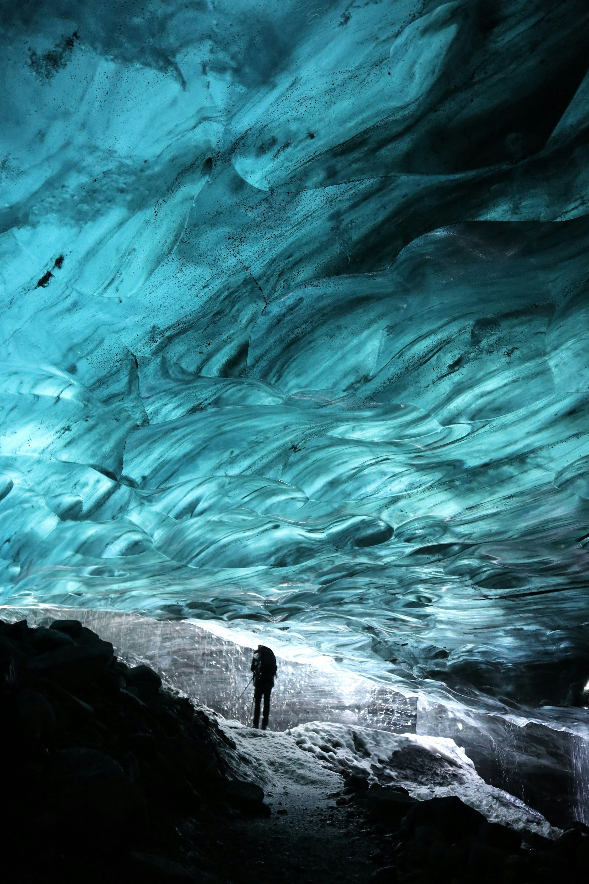 Person in silhouette stands under the Blue Ice Caves, Iceland.