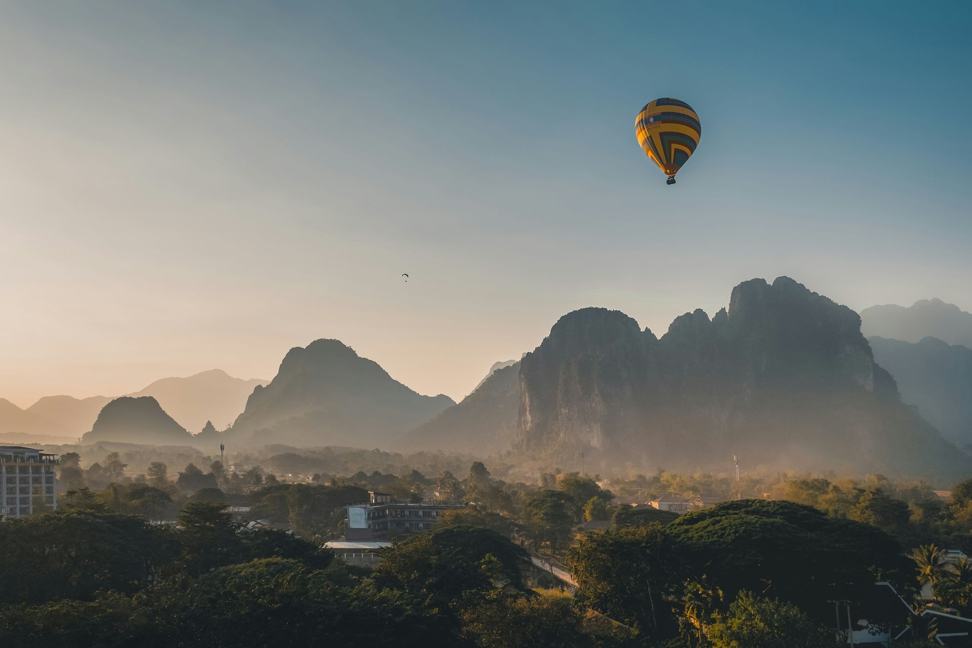 Yellow hot air balloon over mountain range and town at sunrise in Vang Vieng, Laos.