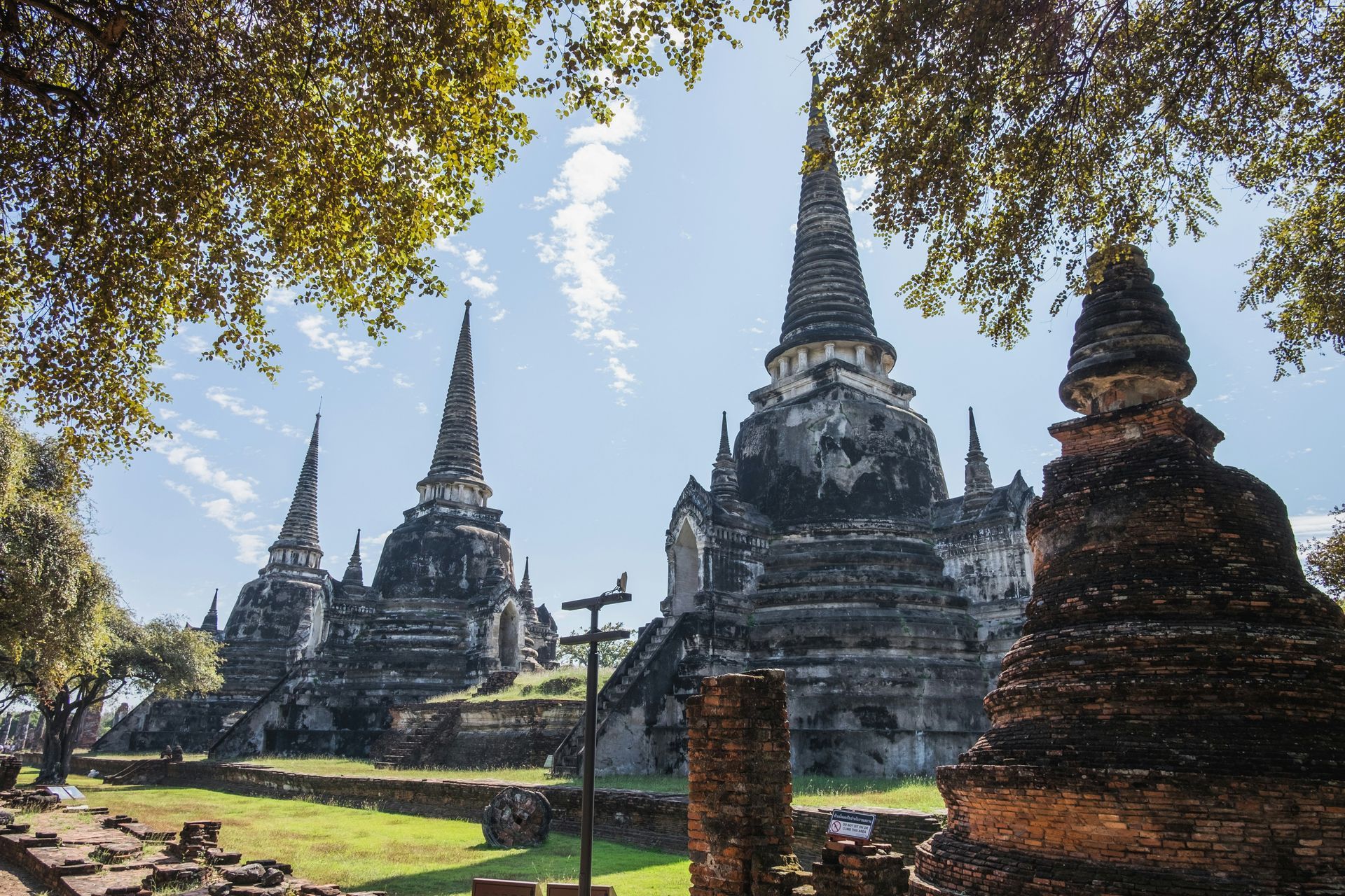 A group of temples are surrounded by trees on a sunny day in Ayutthaya, Thailand.