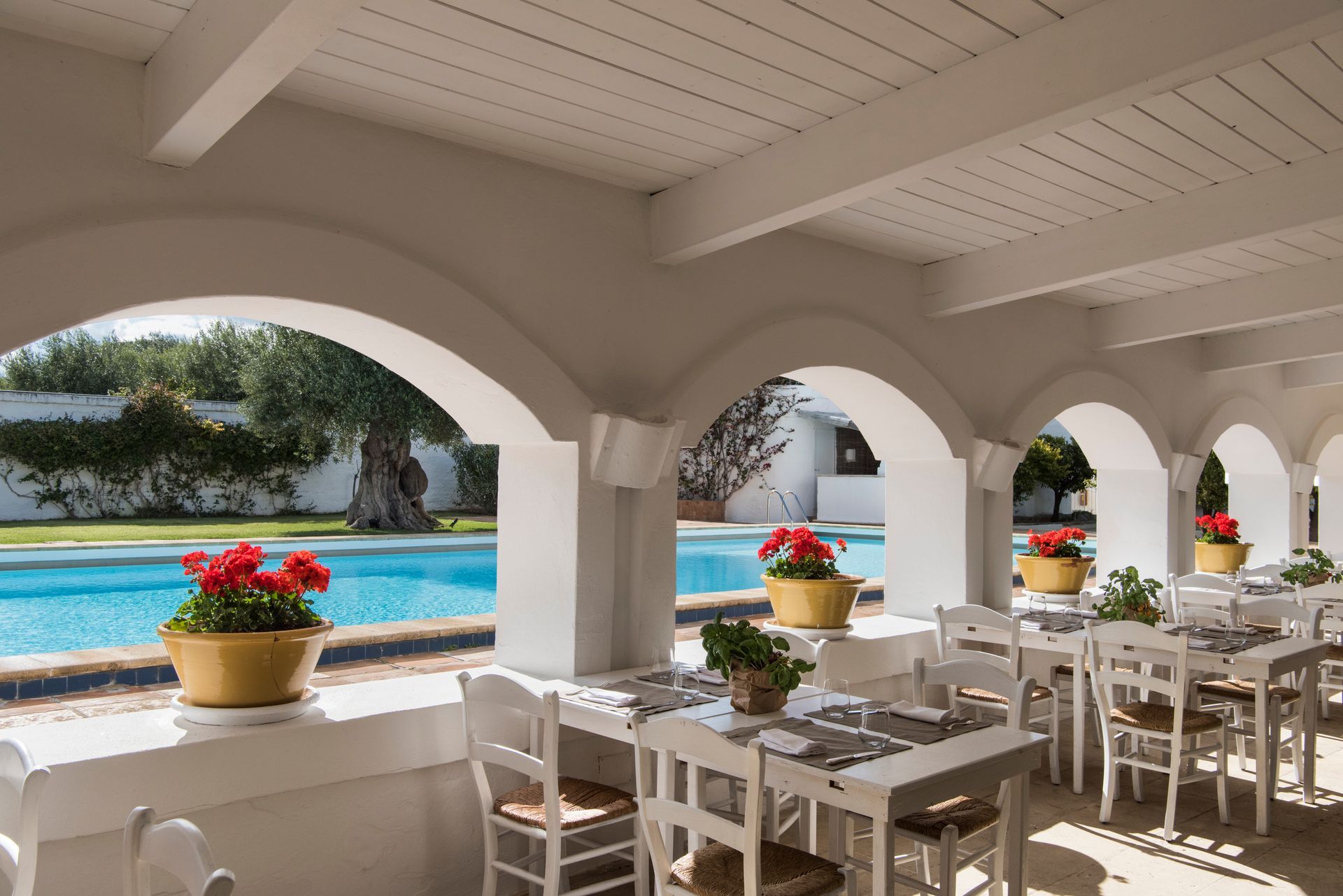 A restaurant with tables and chairs and a pool in the background at Il Melograno Hotel in Puglia, Italy.