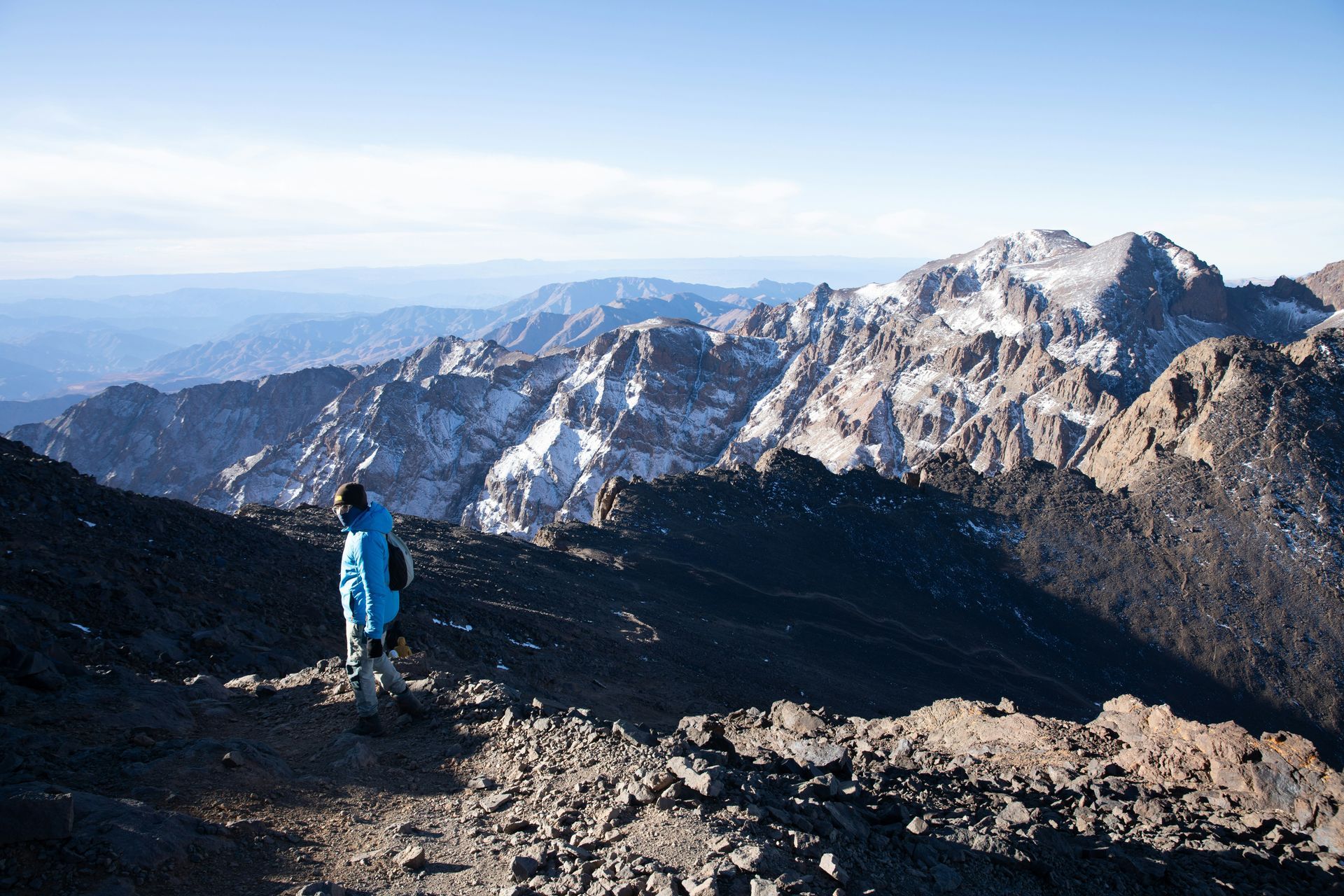 A person in a blue jacket is standing on top of a mountain in Toubkal, Morocco.
