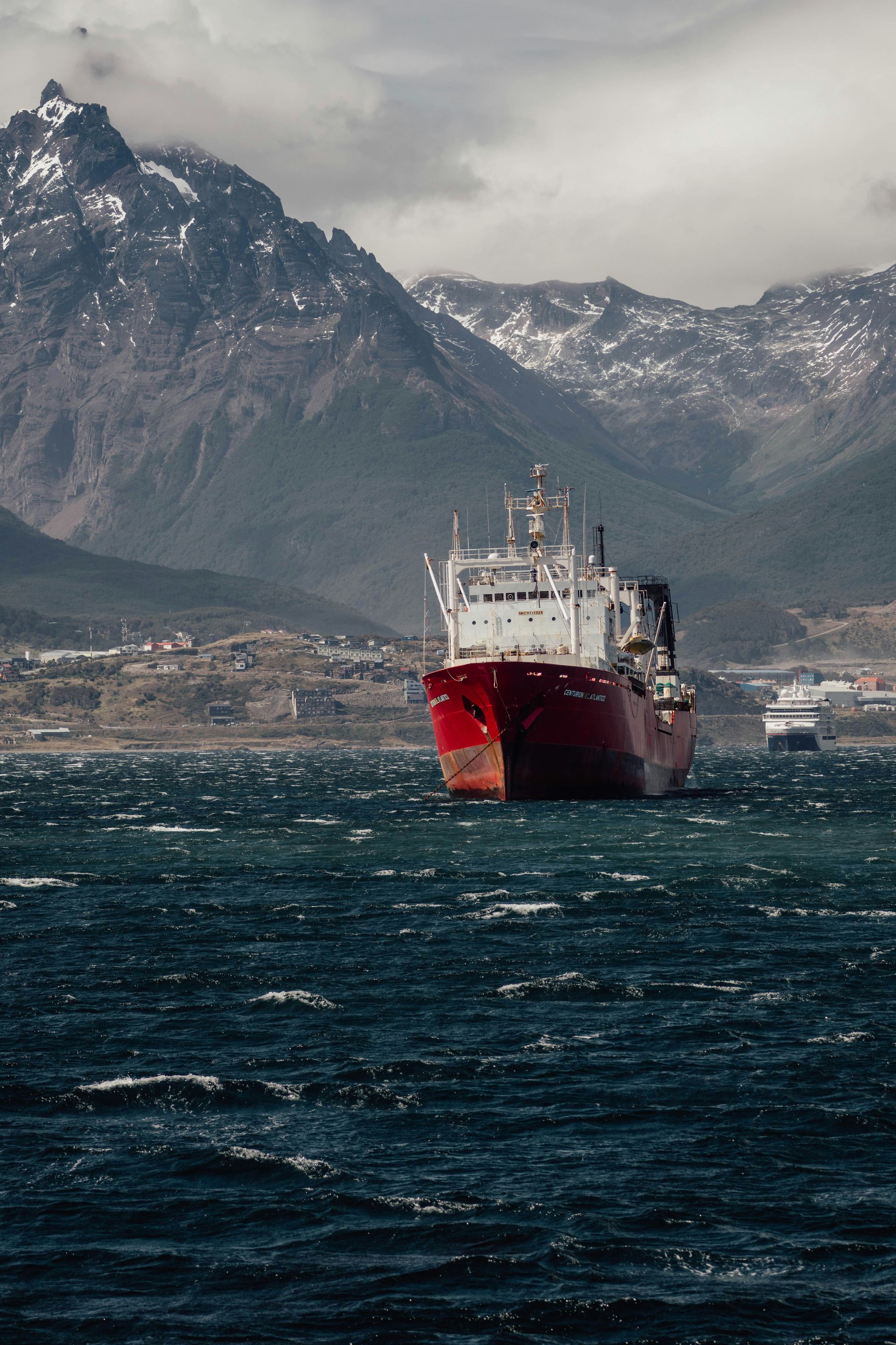 Red ship on choppy water with mountains in the background in Ushuaia, Argentina.