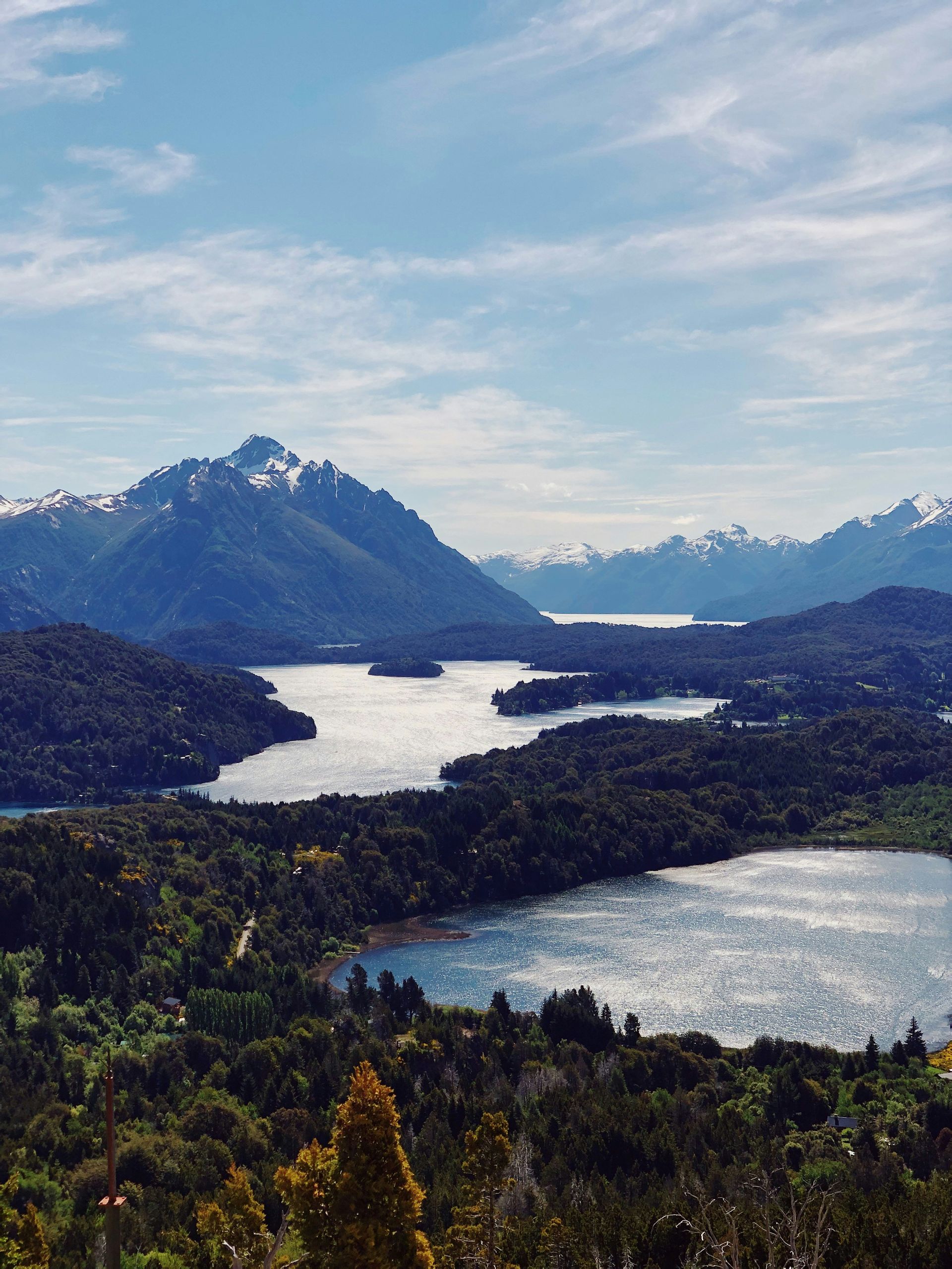 Lakes and forest under a bright sky with snow-capped mountains in the distance in San Carlos de Bariloche, Argentina.