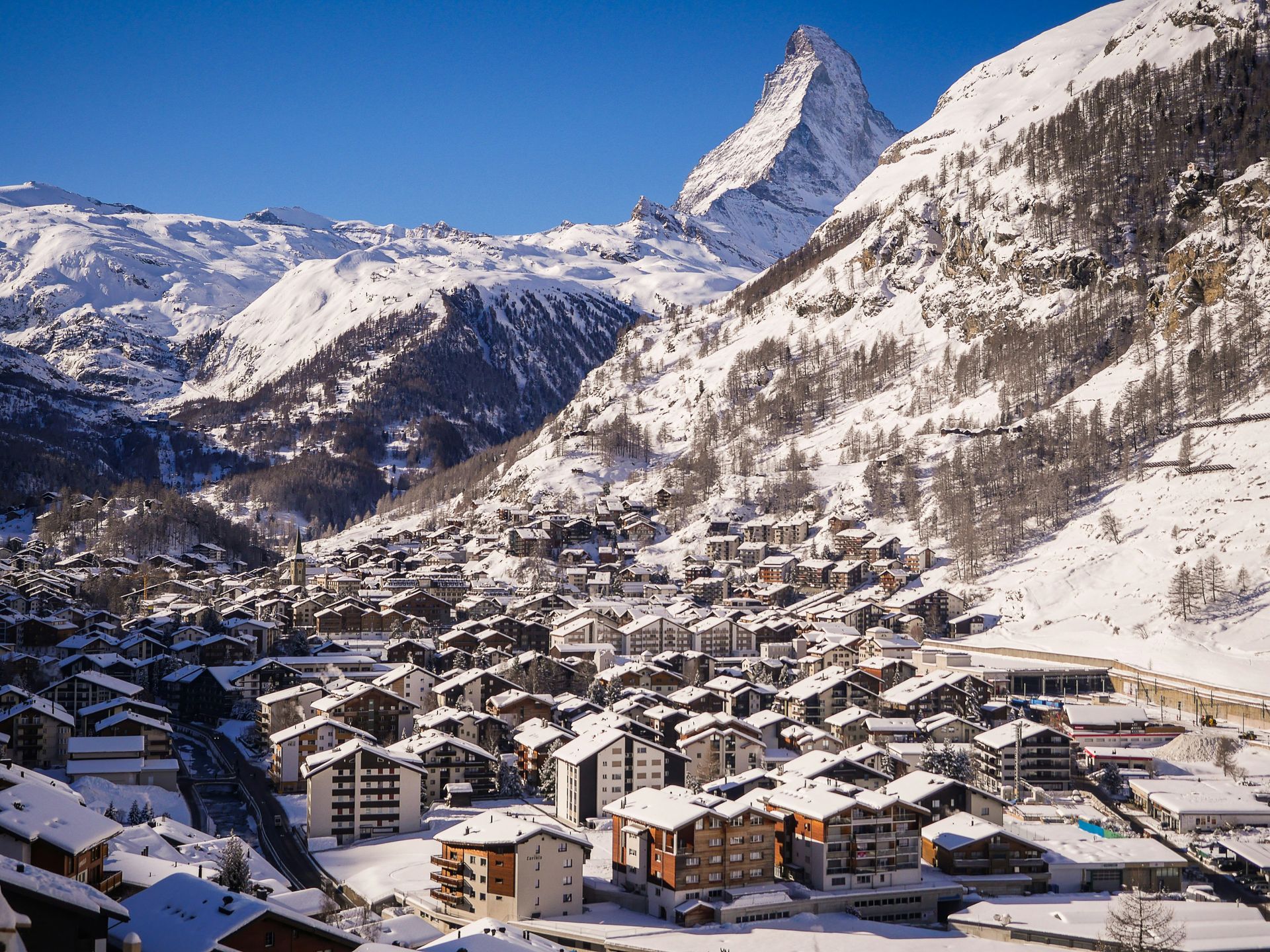 Snowy mountain town with Matterhorn peak under a bright blue sky in Zermatt, Switzerland.