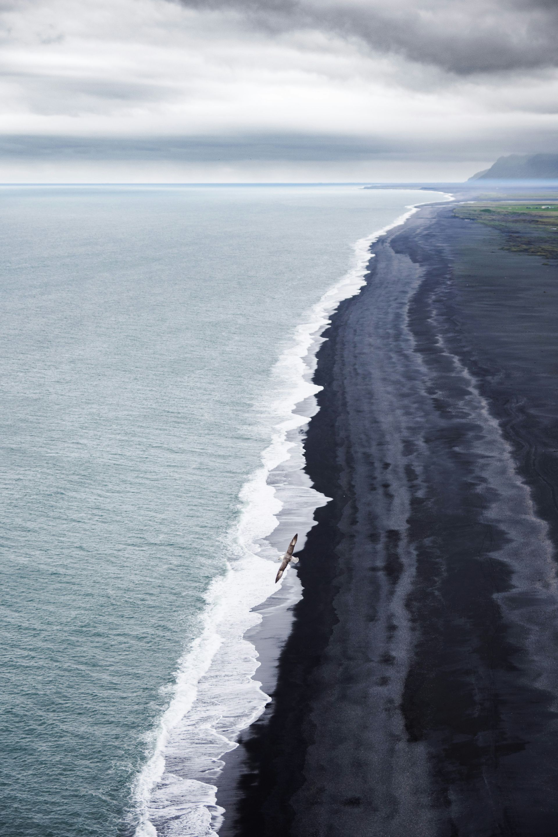 Black sand beach meets ocean under a cloudy sky on Reynisfjara Beach, Iceland.