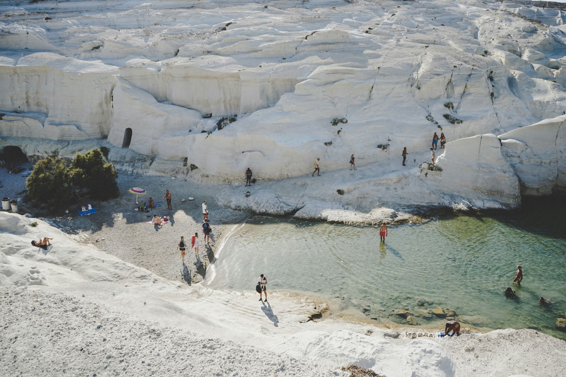 A group of people are standing on a beach next to a body of water in Milos, Greece.