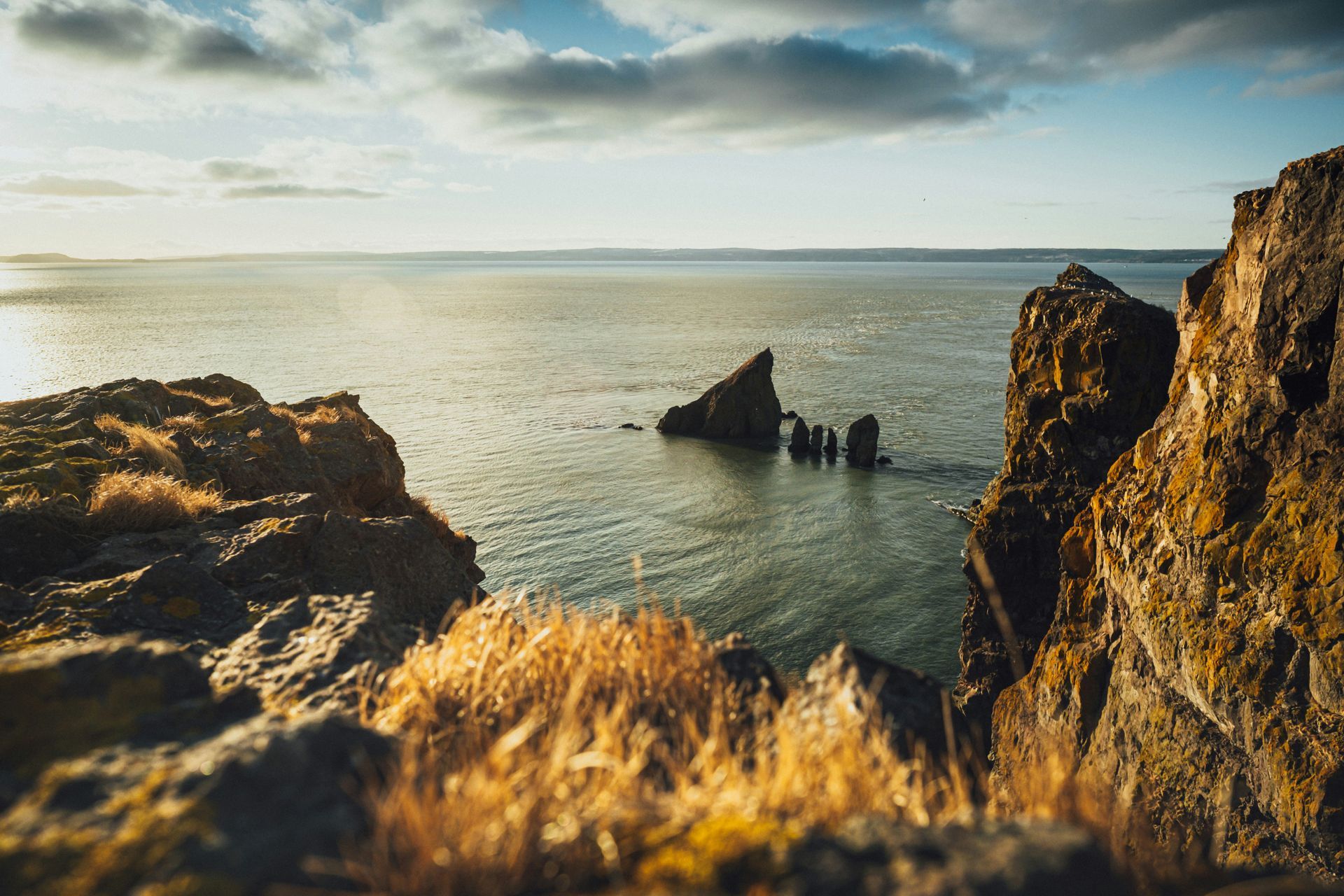 Rocky cliffs overlooking a calm sea under a partly cloudy sky; golden light in Nova Scotia, Canada.
