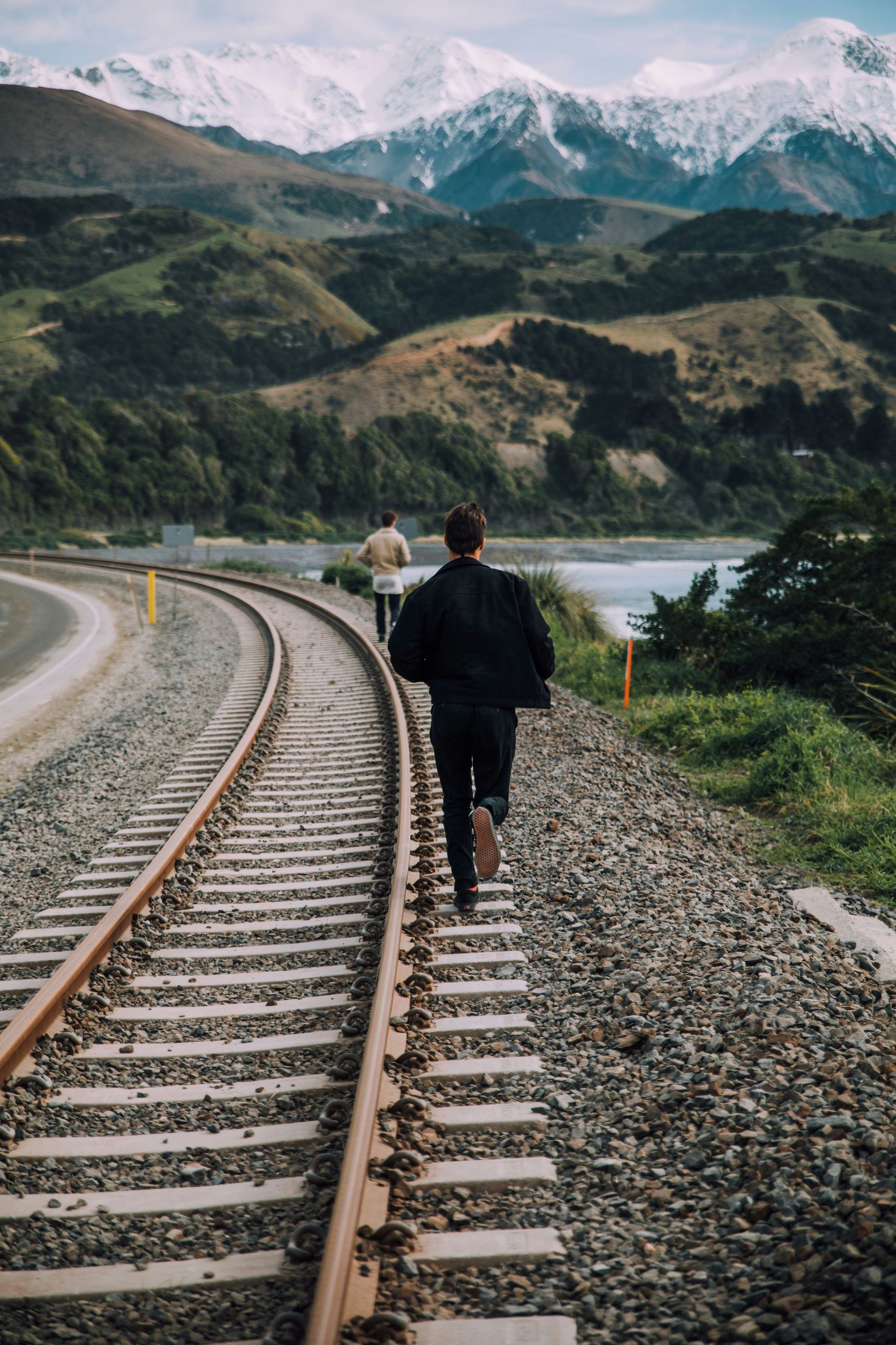 A man is walking down train tracks with mountains in the background in Kaikōura, New Zealand.
