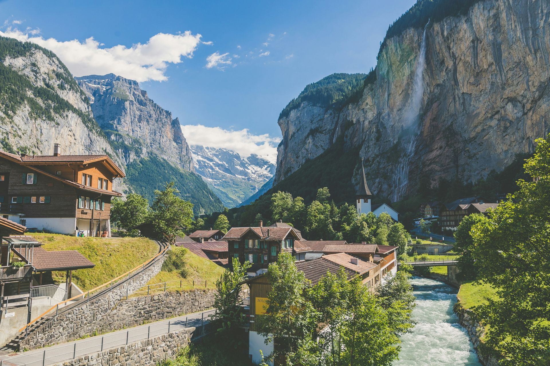 A Swiss village nestled between mountains with a river, under a blue sky in Lauterbrunnen.