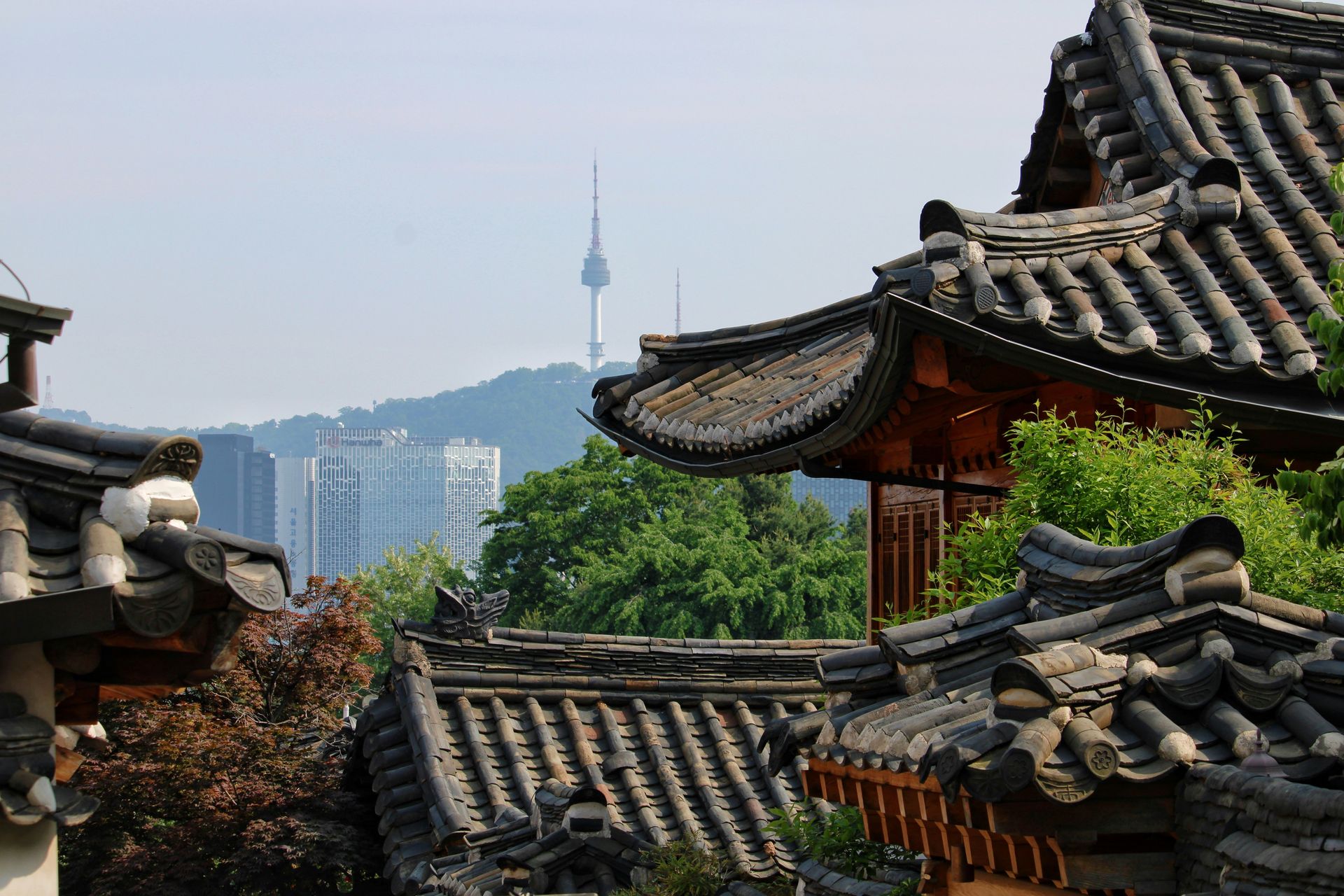 Traditional Korean rooftops frame a view of modern Seoul, with the N Seoul Tower in the distance.