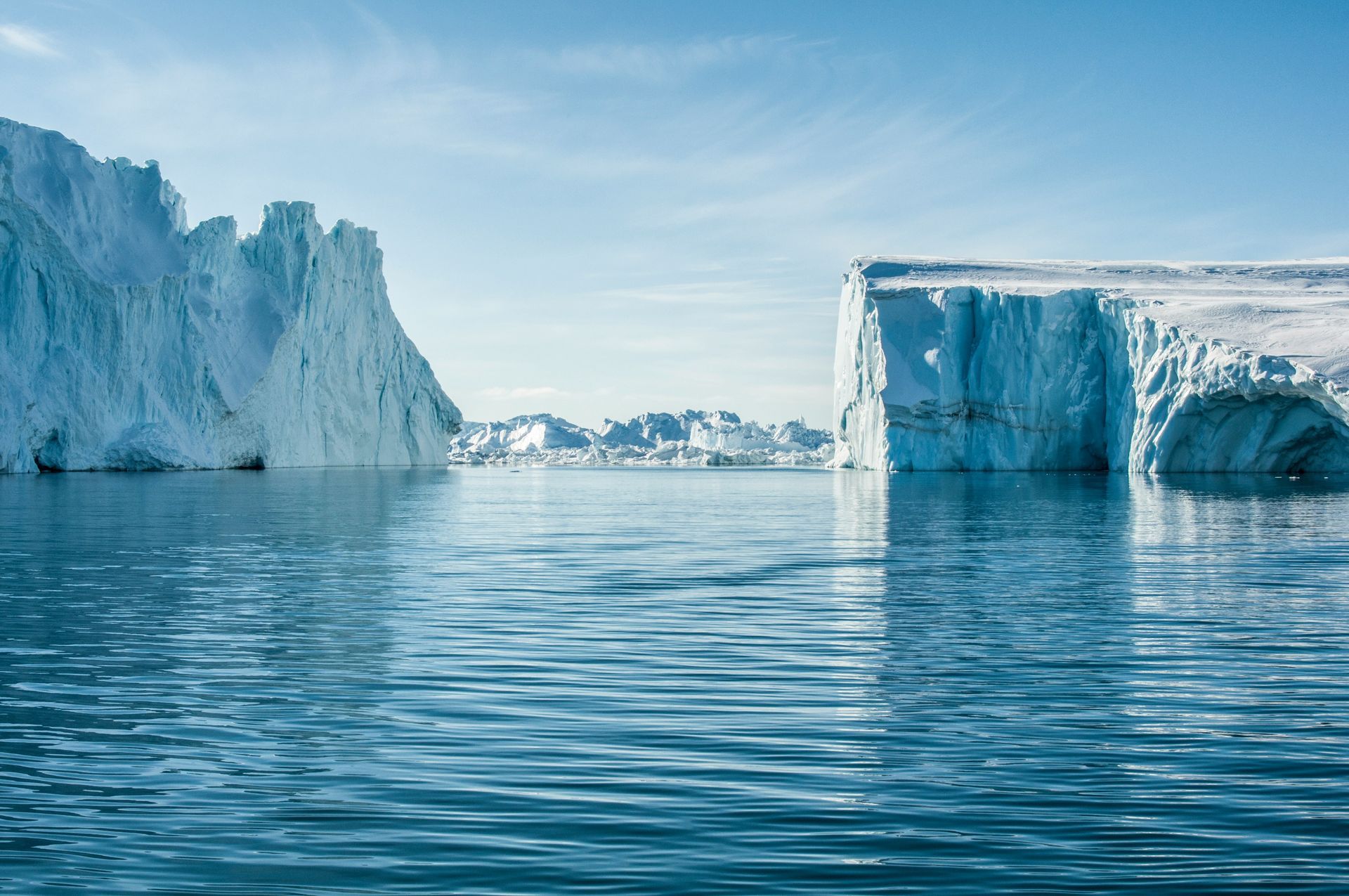 Icebergs floating in blue water under a clear sky at the Ilulissat Icefjord, Greenland.