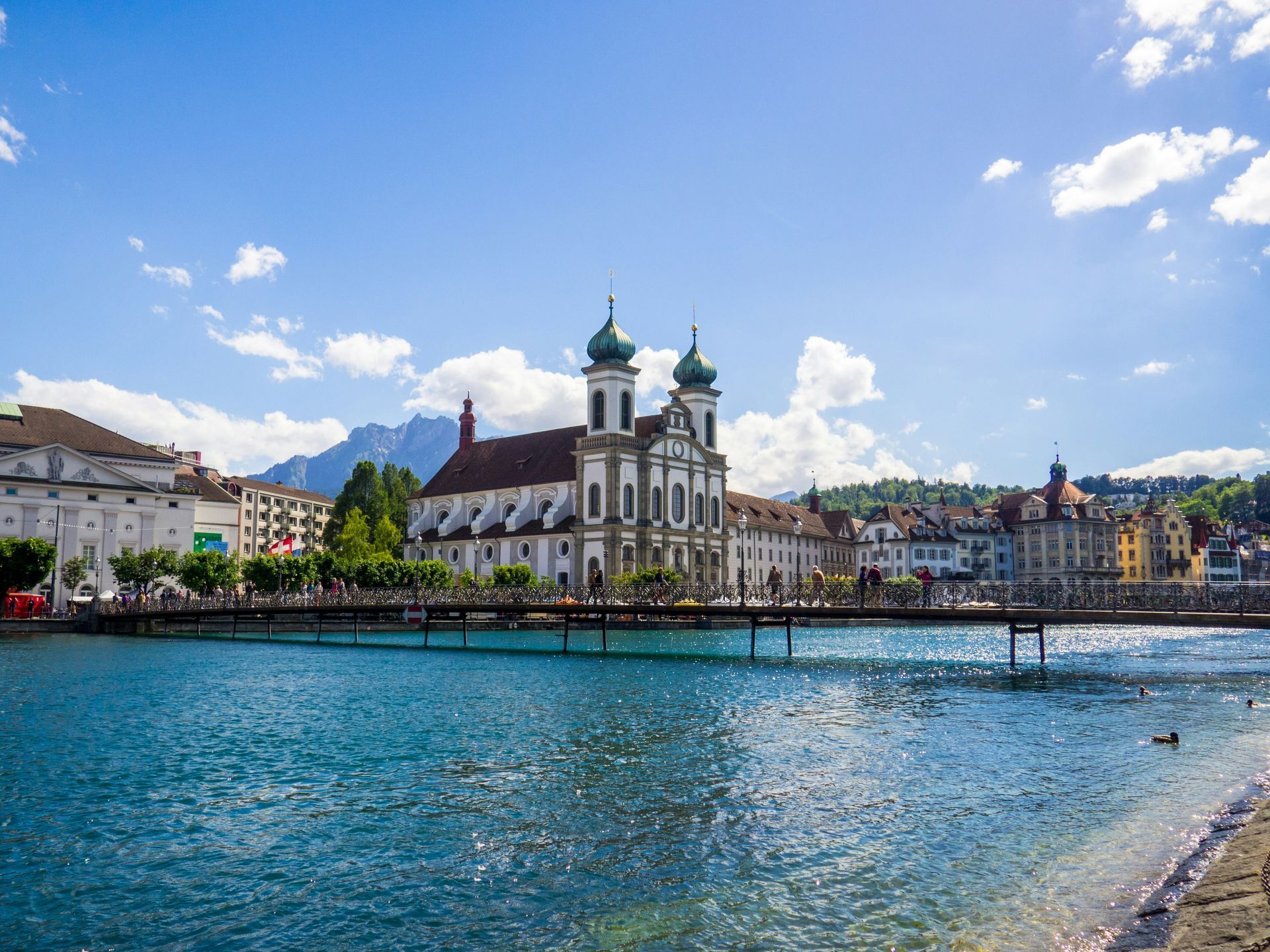 A scenic view of Lucerne, Switzerland with a church, blue lake, and mountains.