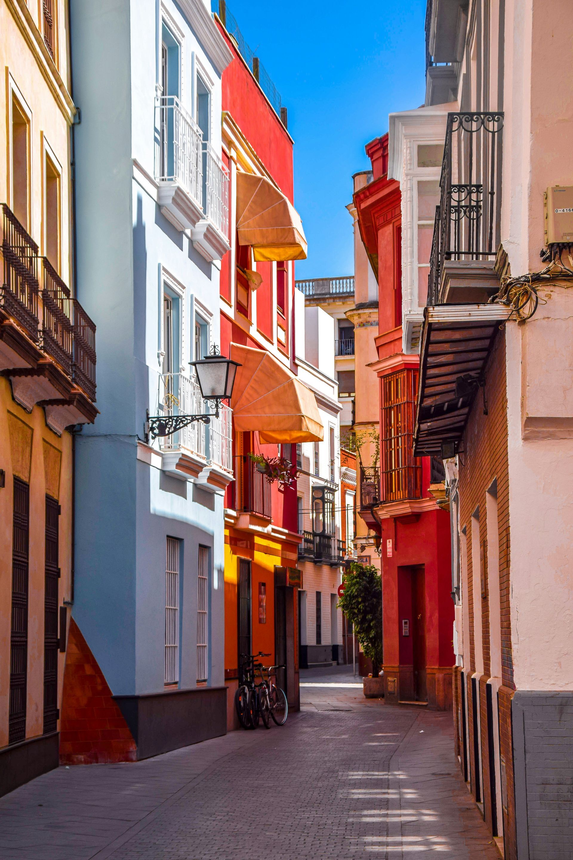 Narrow, colorful street in Seville, Spain; buildings painted in blue, red, orange, and yellow.