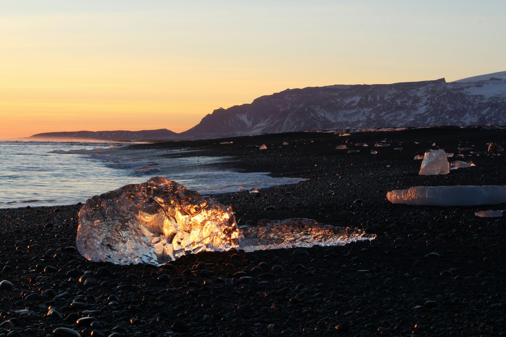 Icebergs on black sand beach at sunrise, with mountains in the background at Diamond Beach, Iceland.