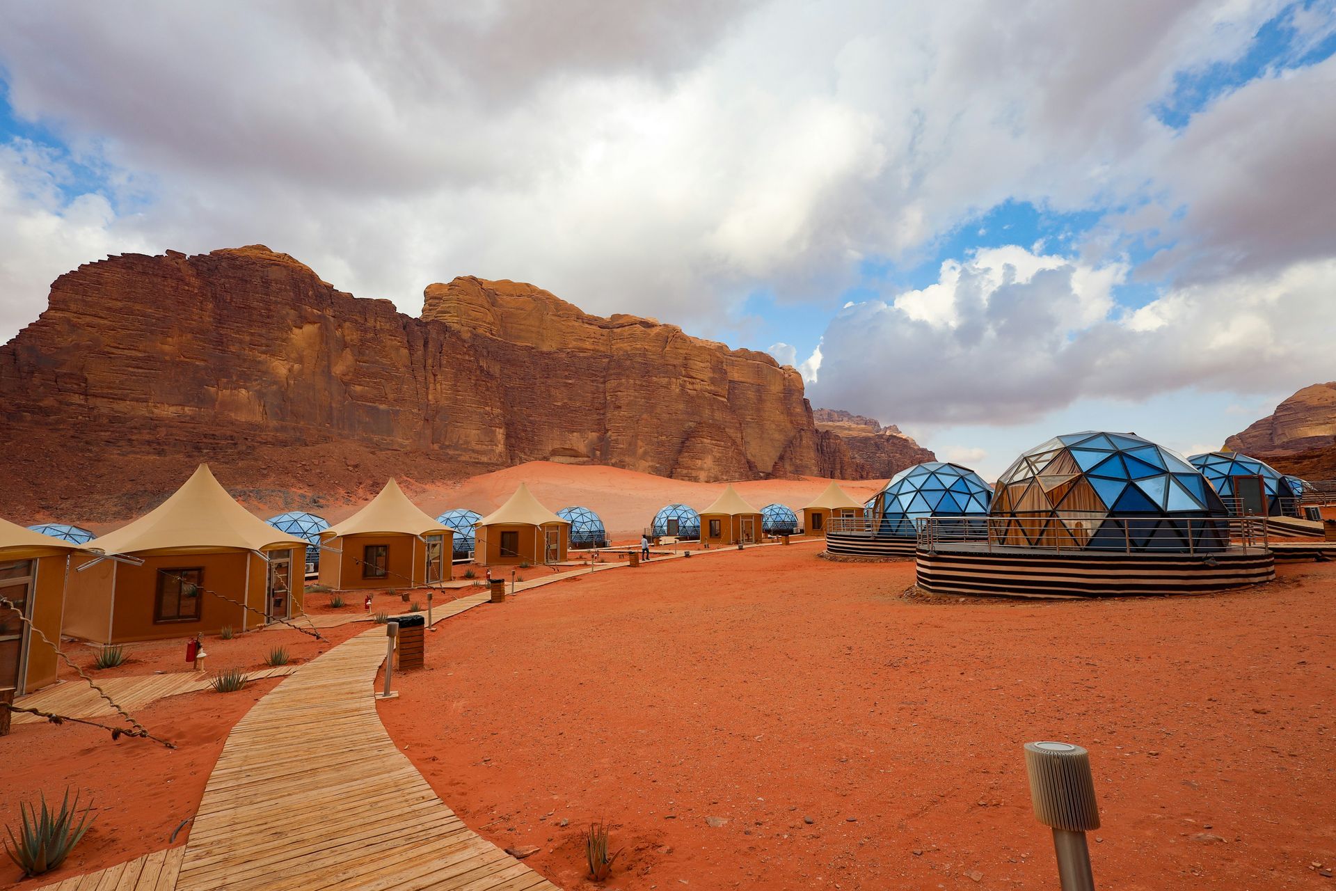 Desert resort with beige tents and blue dome structures against red rock formations in Wadi Rum, Jordan.