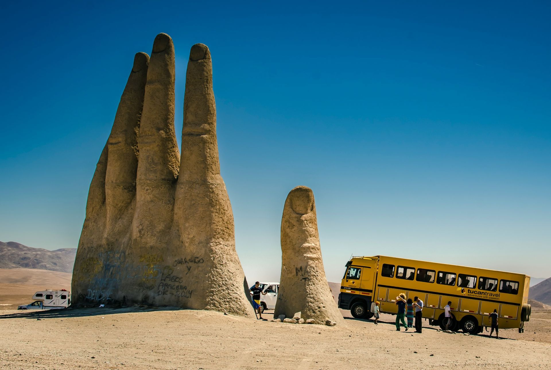 The Atacama Desert, Chile with giant hand sculpture; yellow school bus and people gather.