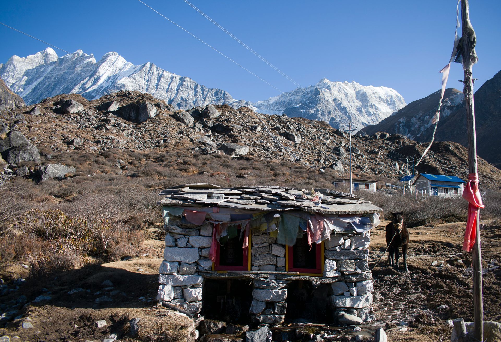 Stone structure with red-framed windows in a mountain landscape, snow-capped peaks in Langtang, Nepal.
