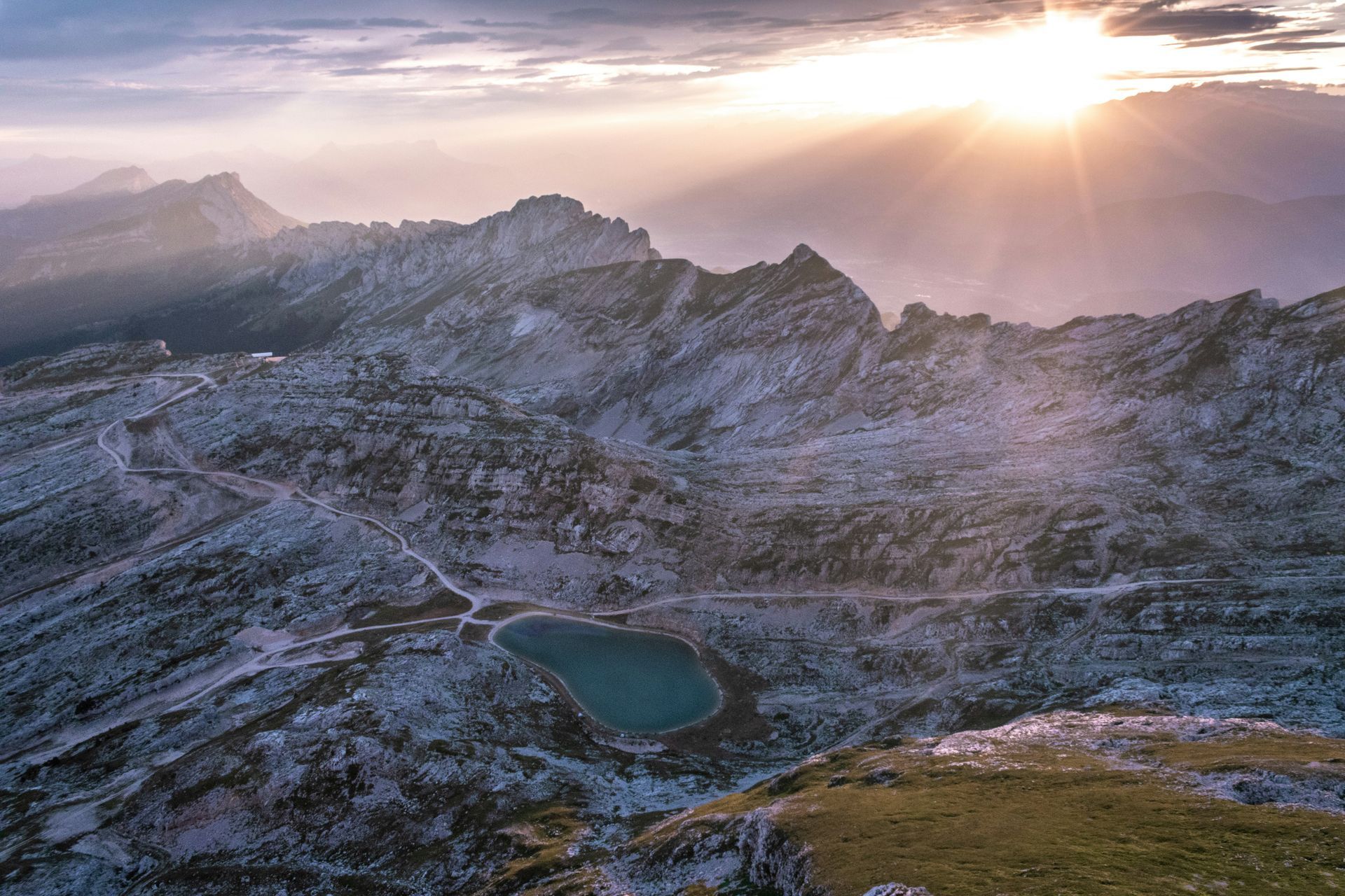 The sun is shining through the clouds over a mountain range with a lake in the middle in Grenoble, France.