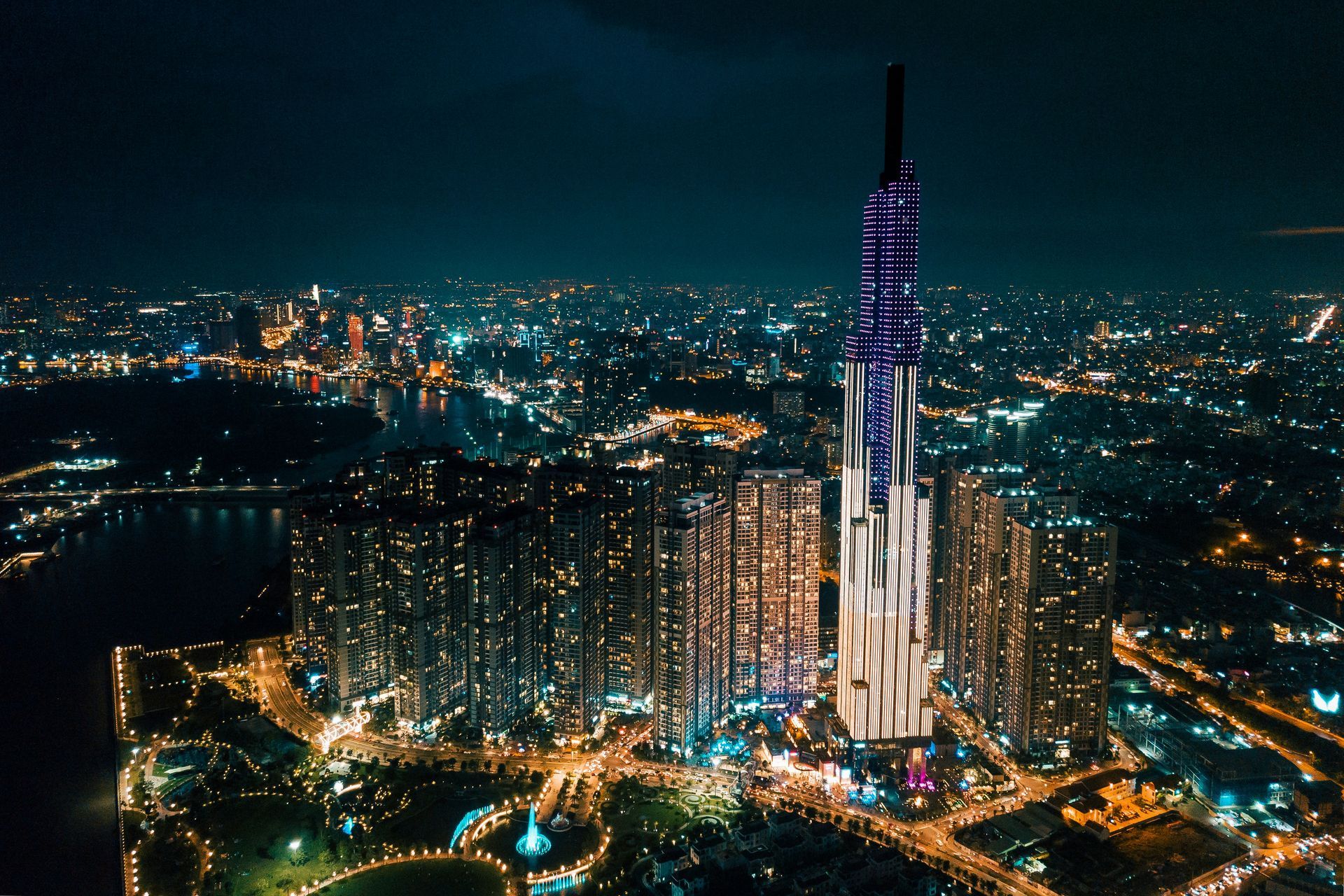 Night aerial view of Ho Chi Minh City skyline with the Landmark 81 skyscraper illuminated in blue, white, and gold.