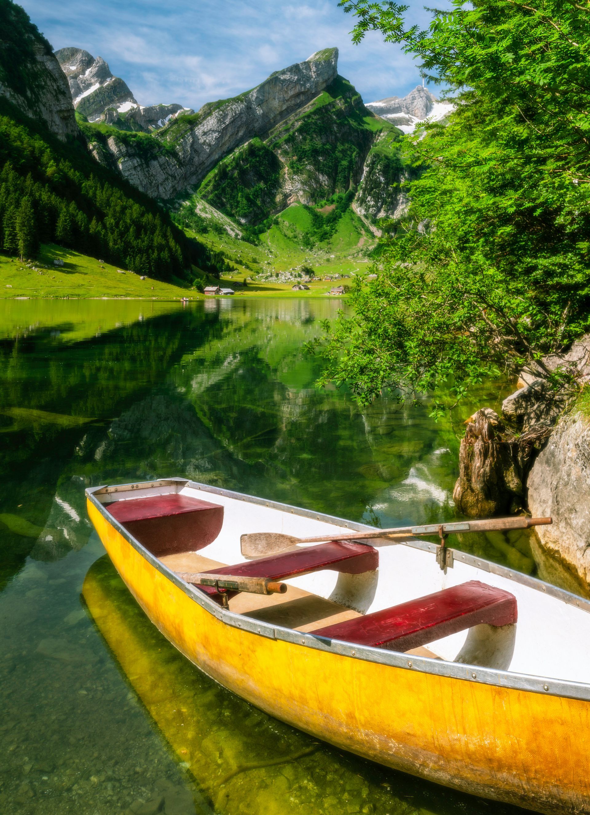 Yellow rowboat on a calm lake, reflecting mountains and green landscape in Schwende, Switzerland.