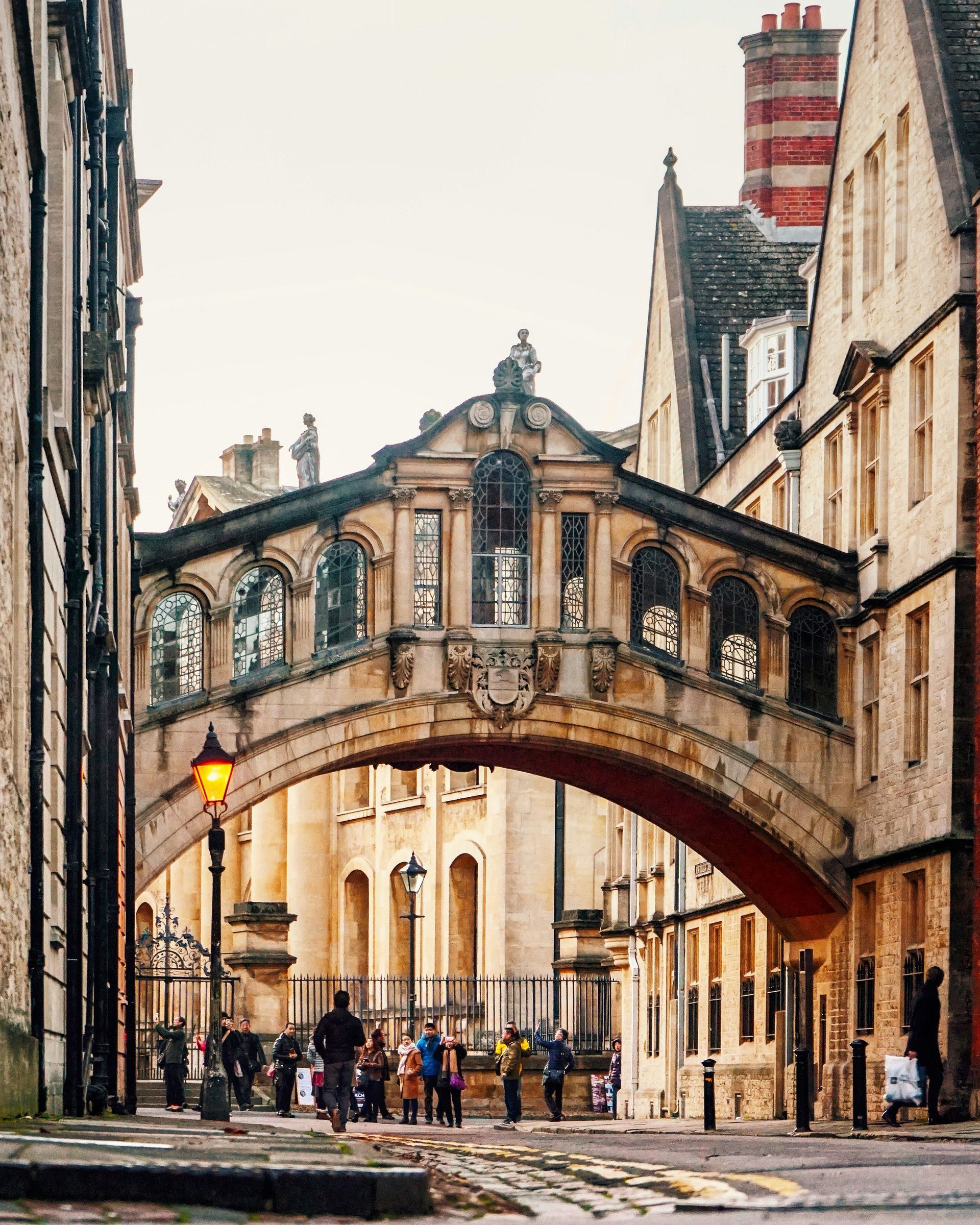 Bridge of Sighs, Oxford, UK. Arched sandstone bridge spans street between buildings; people walking below.