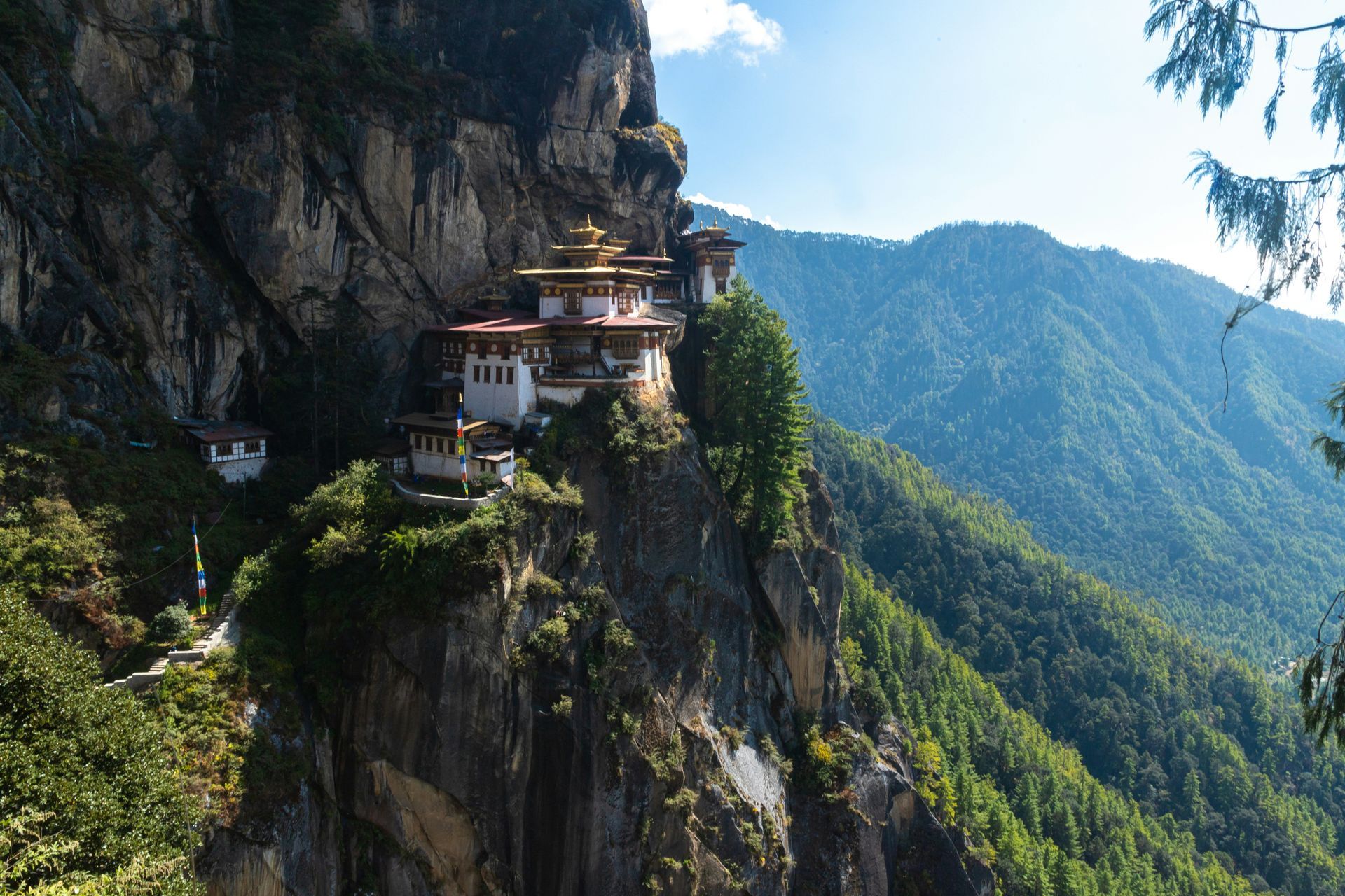 Tiger’s Nest Monastery, Bhutan, perched on a cliff face. White buildings with gold roofs against a green mountain.