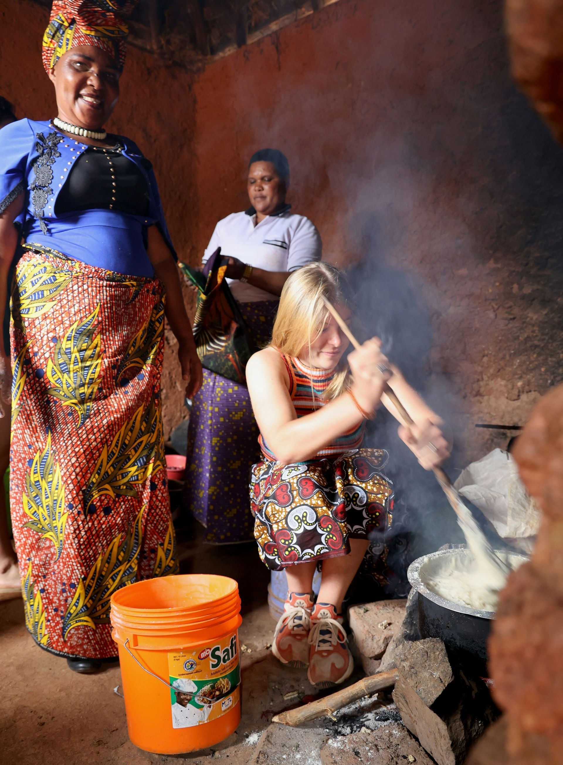 A woman is stirring something in a pot next to an orange bucket in Tanzania.