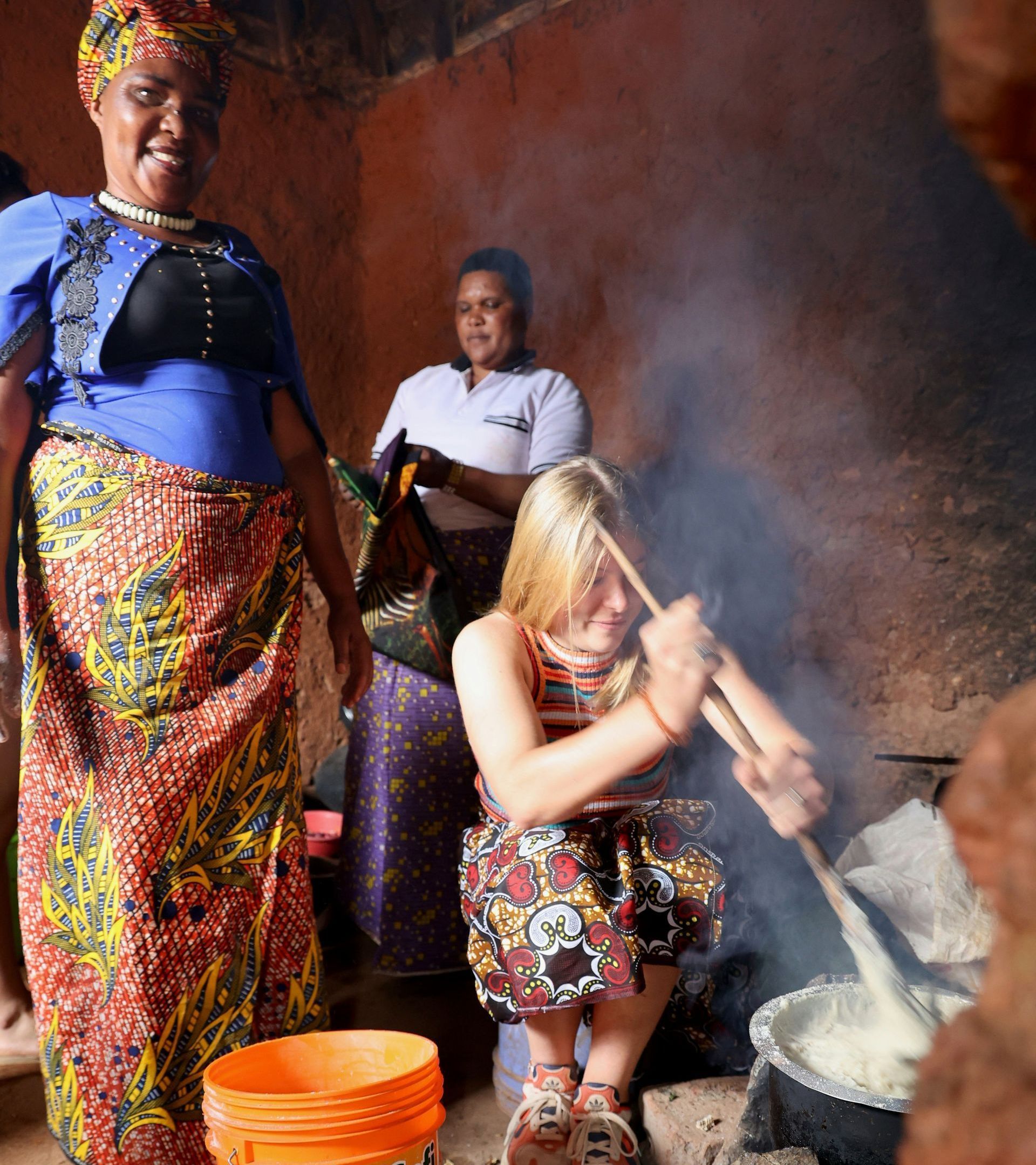 A woman is stirring something in a pot next to an orange bucket in Tanzania.