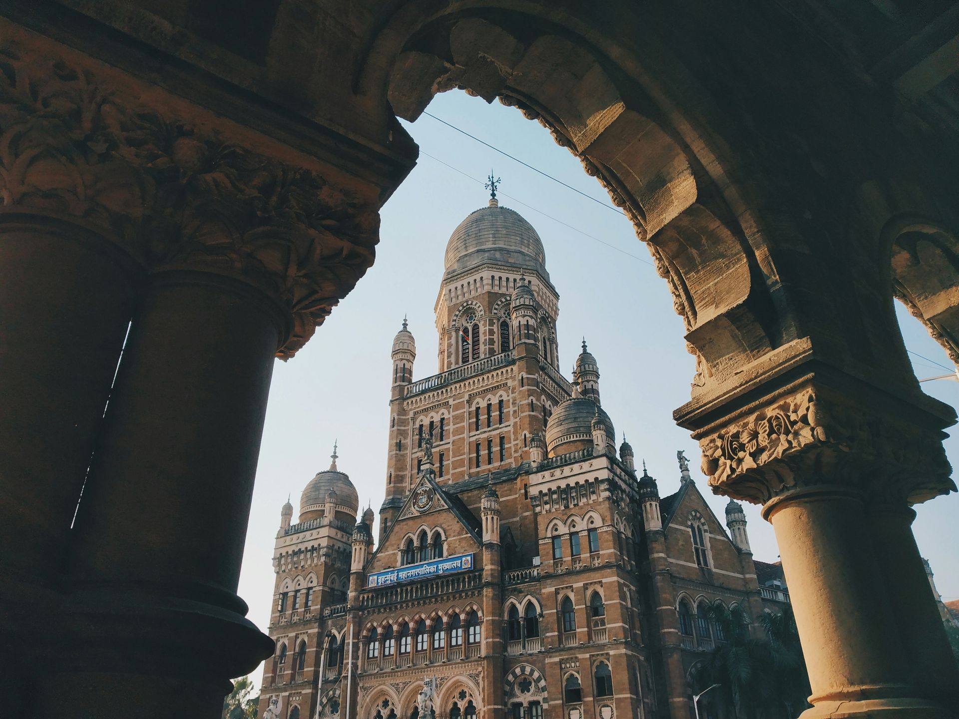 Mumbai's municipal building framed by ornate archway.  Brown stone building with a dome against a blue sky.