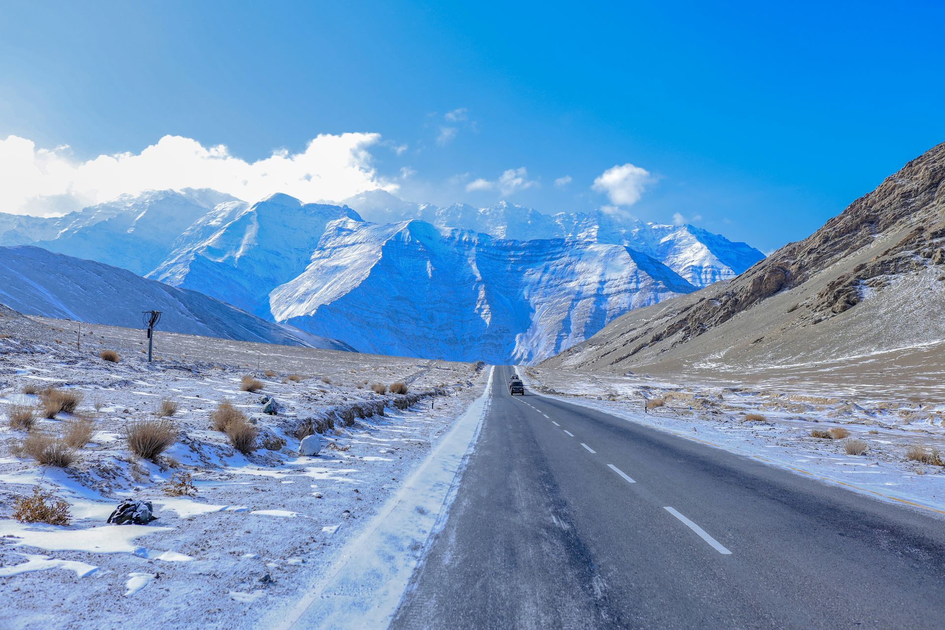Snowy mountain road with car. Mountains in the background, fields of snow on the side in Ladakh, India.