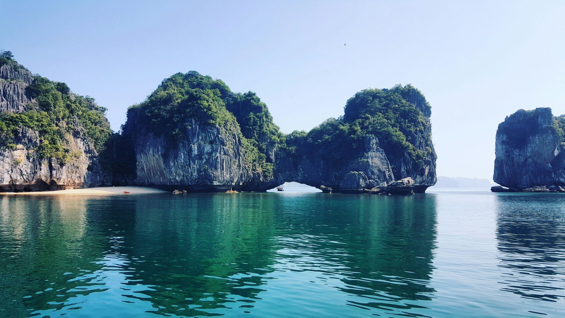 Emerald water surrounds limestone islands with lush green foliage in Halong Bay, Vietnam.