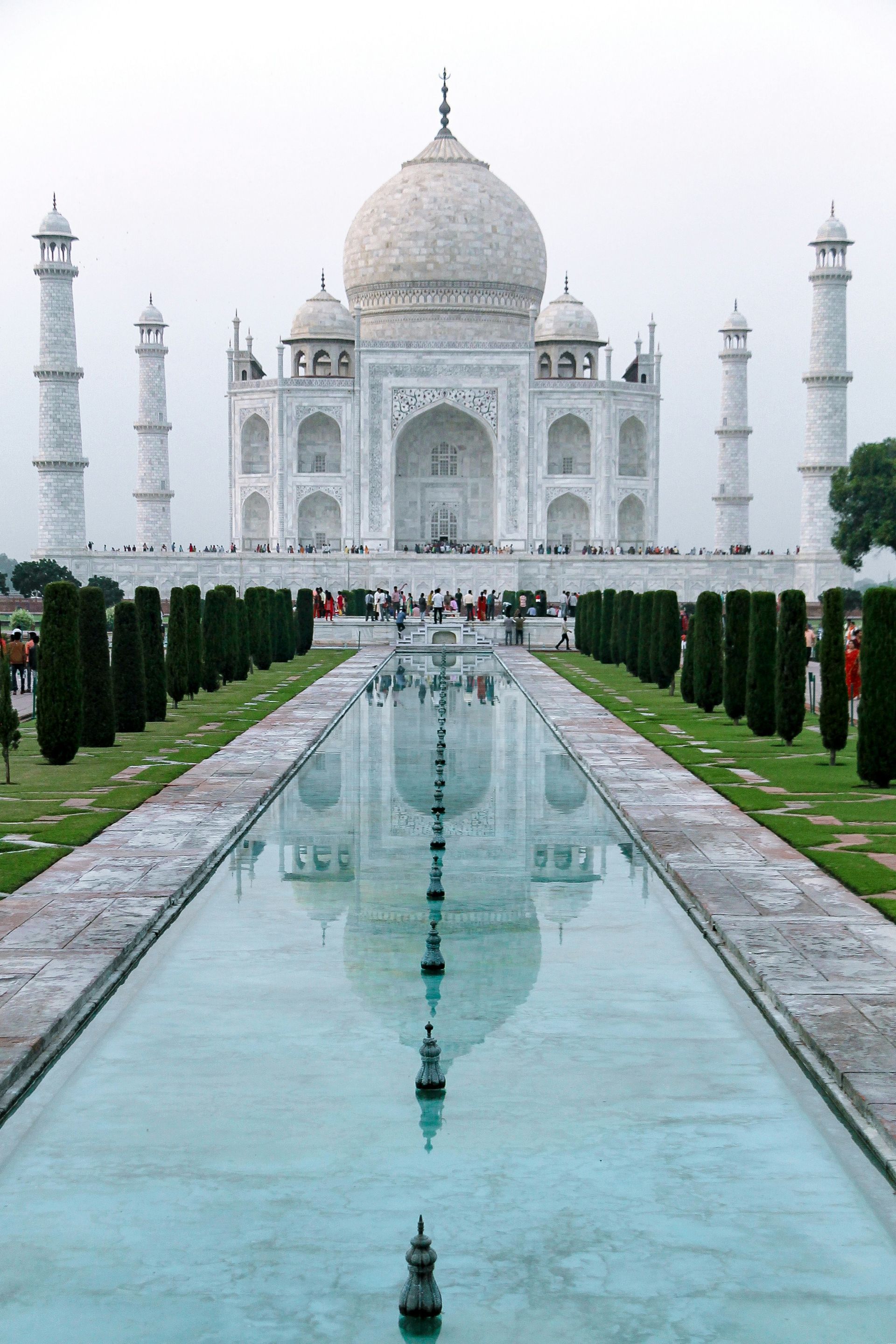Taj Mahal reflecting in a long pool of water. White marble building with four towers, set in a garden.