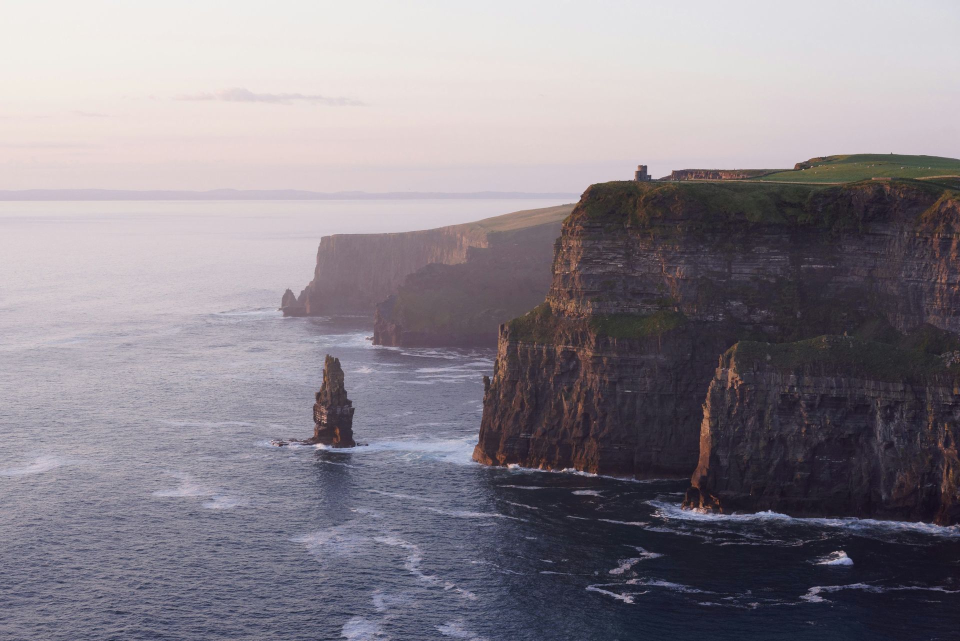Cliffs of Moher along the Irish coast, viewed at sunset, with the ocean and a rock stack.