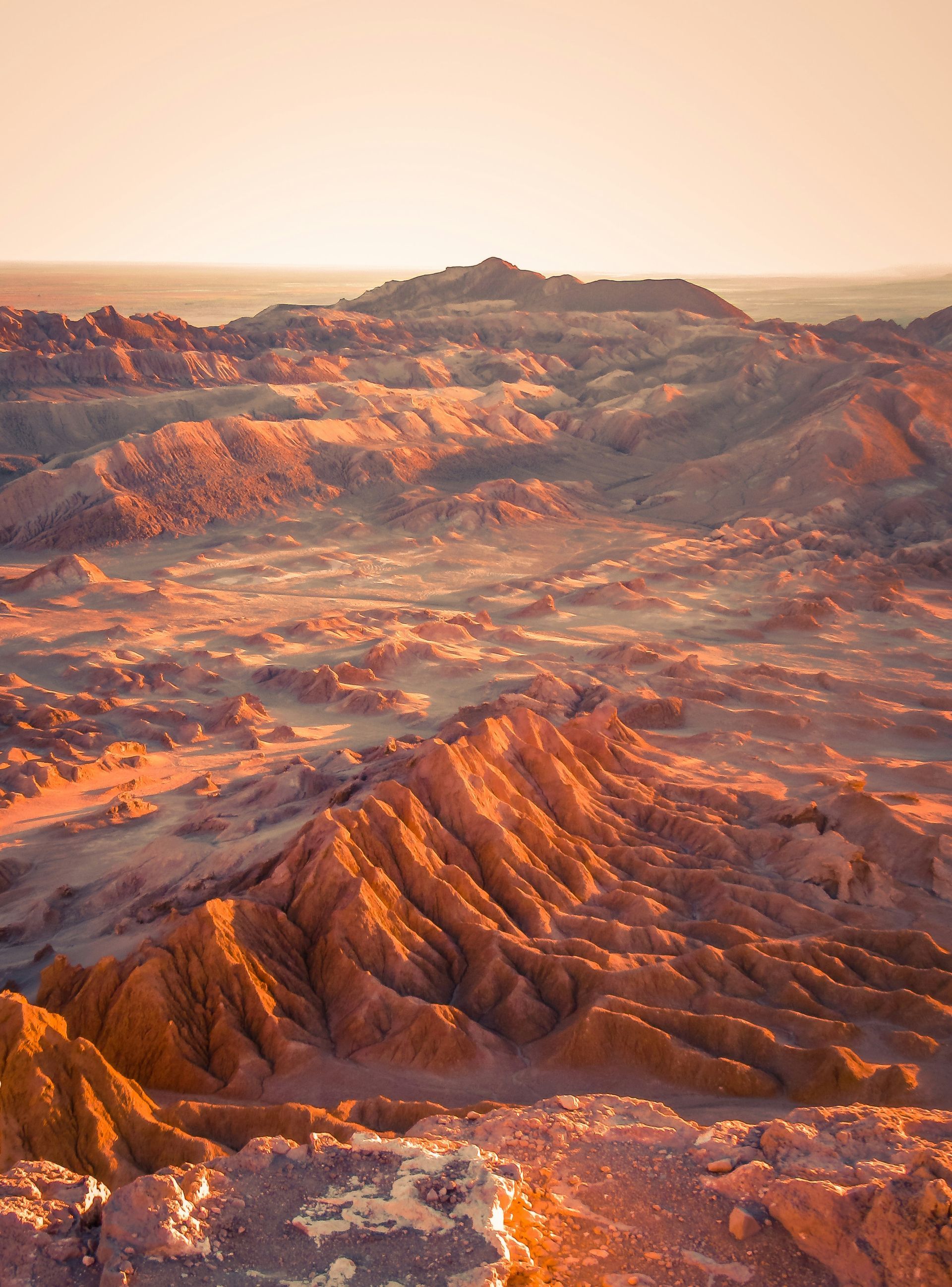 Rocky, desert landscape bathed in warm orange and pink light at sunrise or sunset in the Atacama Desert, Chile.