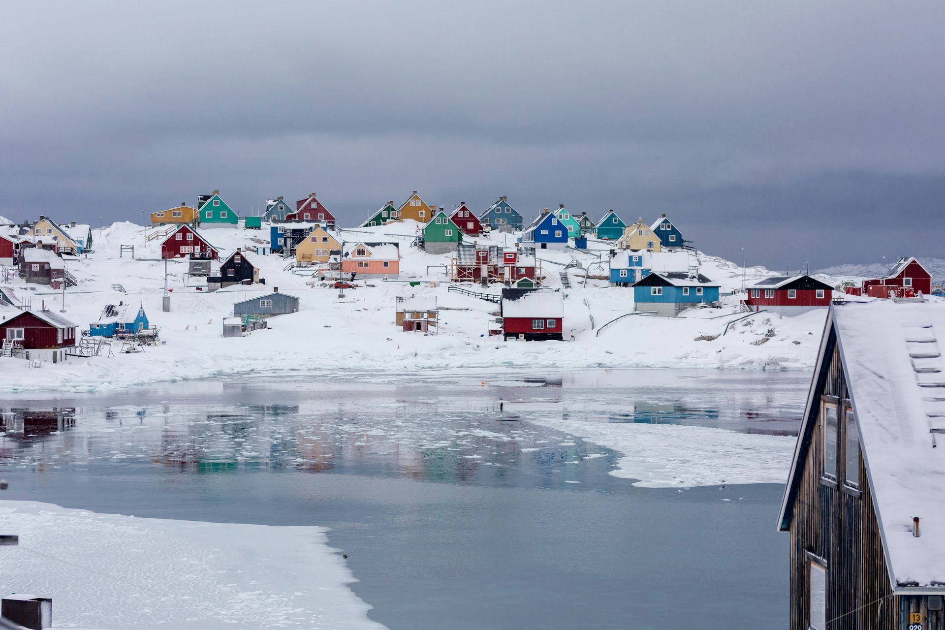 Colorful houses on a snow-covered hill overlooking icy water in Aasiaat, Greenland.