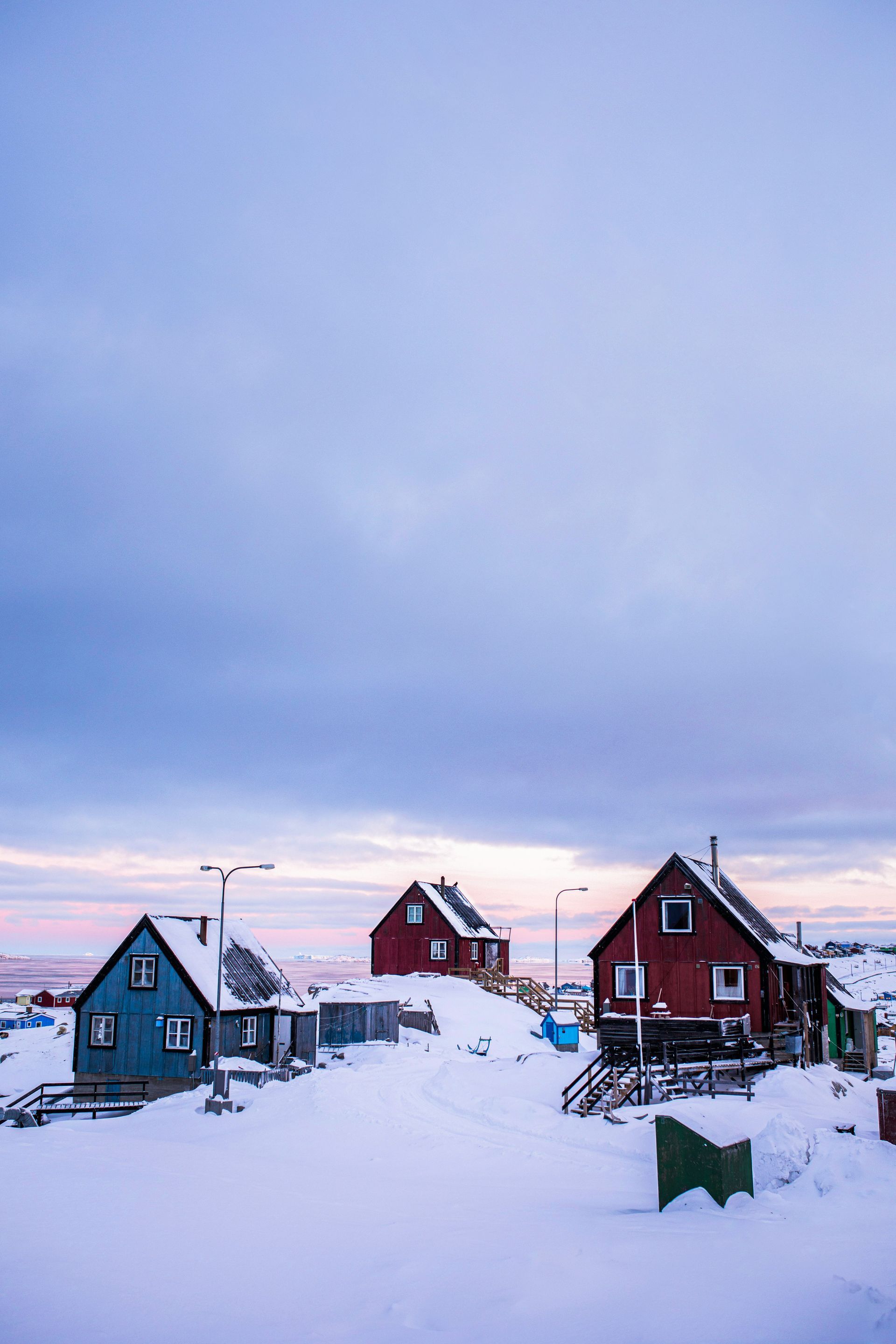 Colorful houses in a snowy landscape under a pale blue and pink sky in Aasiaat, Greenland.