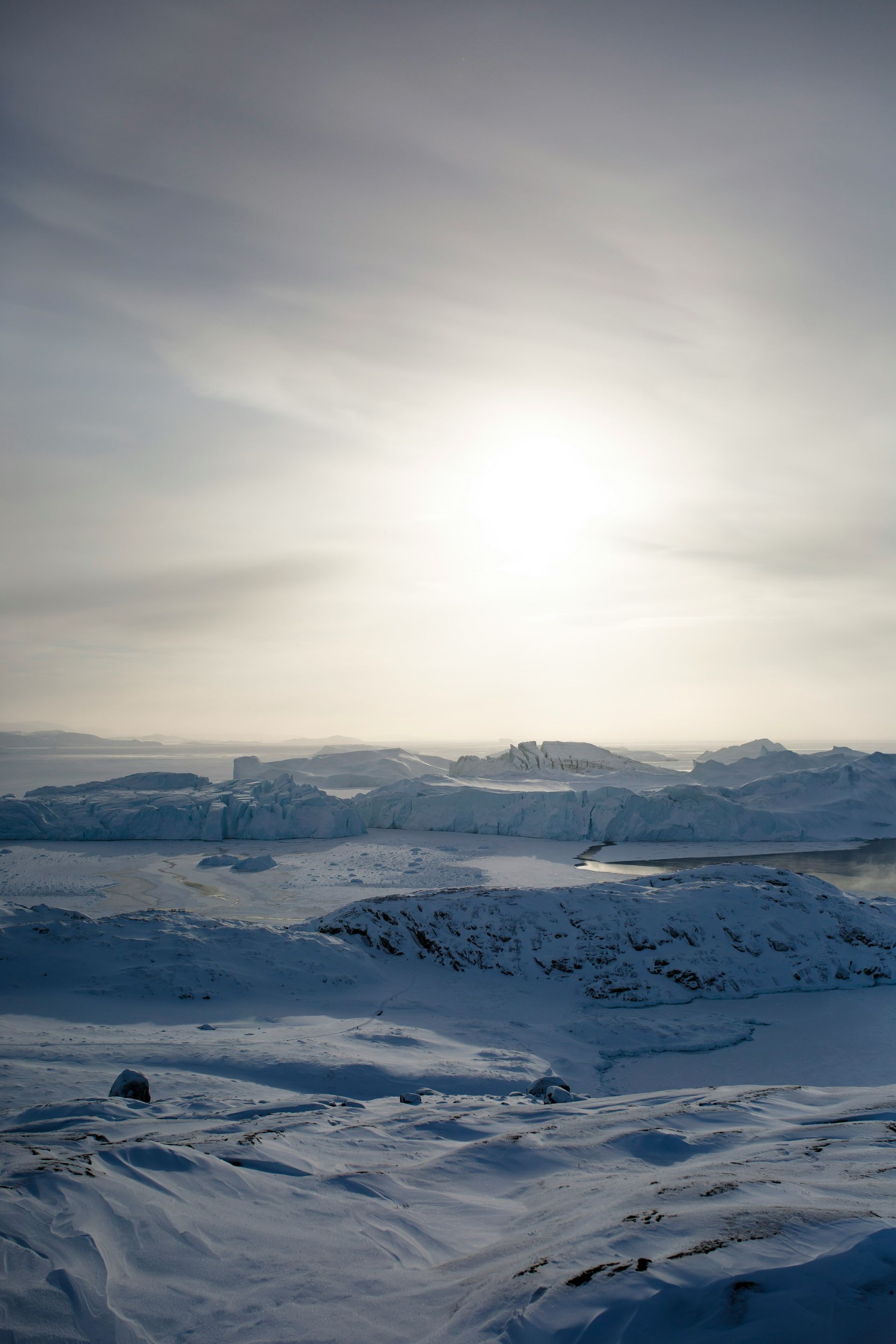 Snowy landscape with bright sun shining over ice formations at the Ilulissat Icefjord, Greenland.
