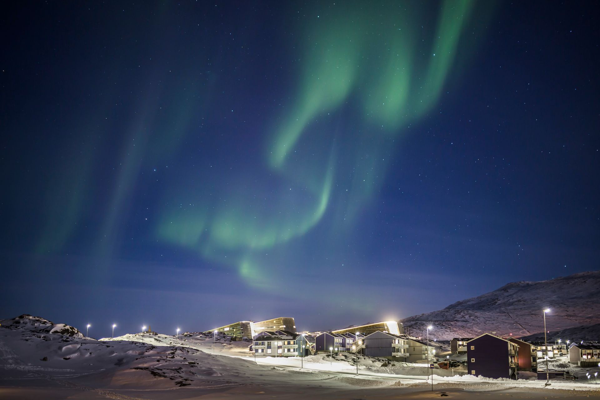 Green aurora borealis over Nuuk, Greenland, at night in a snowy landscape.