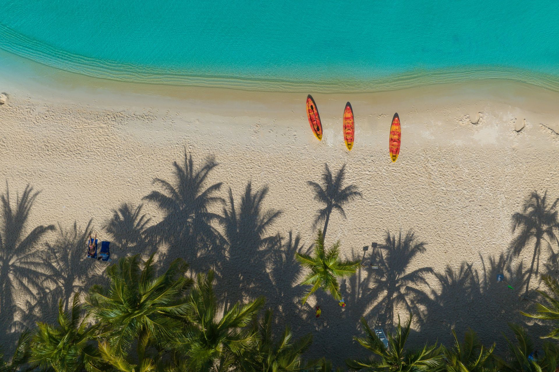 Tropical beach with turquoise water, three kayaks, and shadows of palm trees in Phú Quốc, Vietnam.