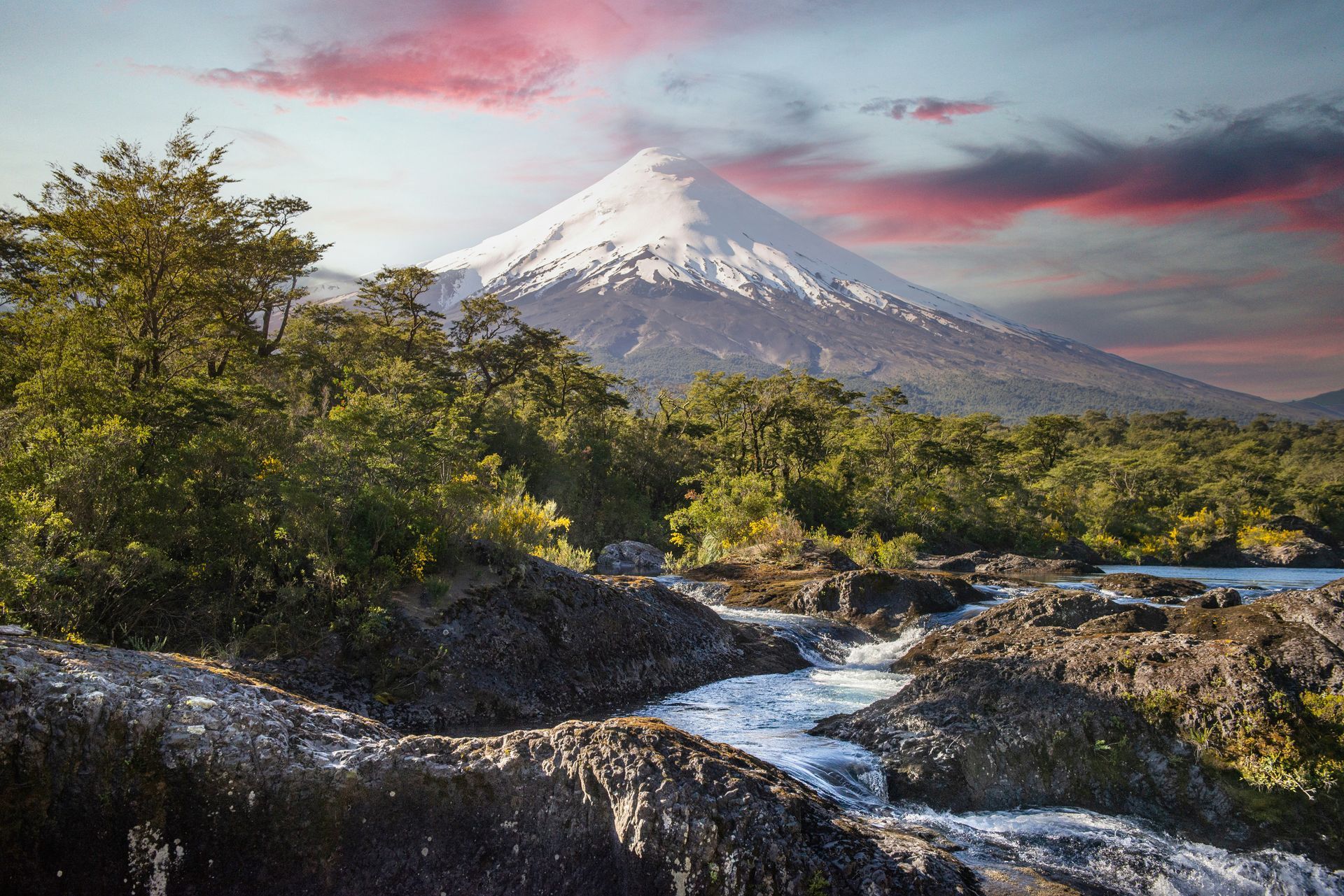 Snow-capped Osorno volcano overlooking a river with the Petrohué Waterfalls at sunset.