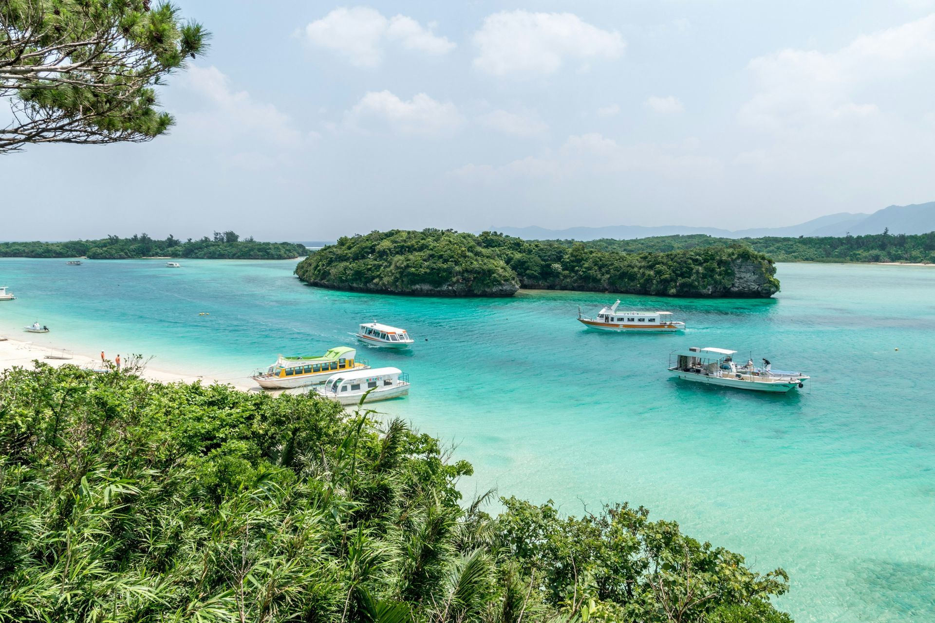 Turquoise ocean with boats, lush green islands, and white sand beach in Okinawa, Japan.