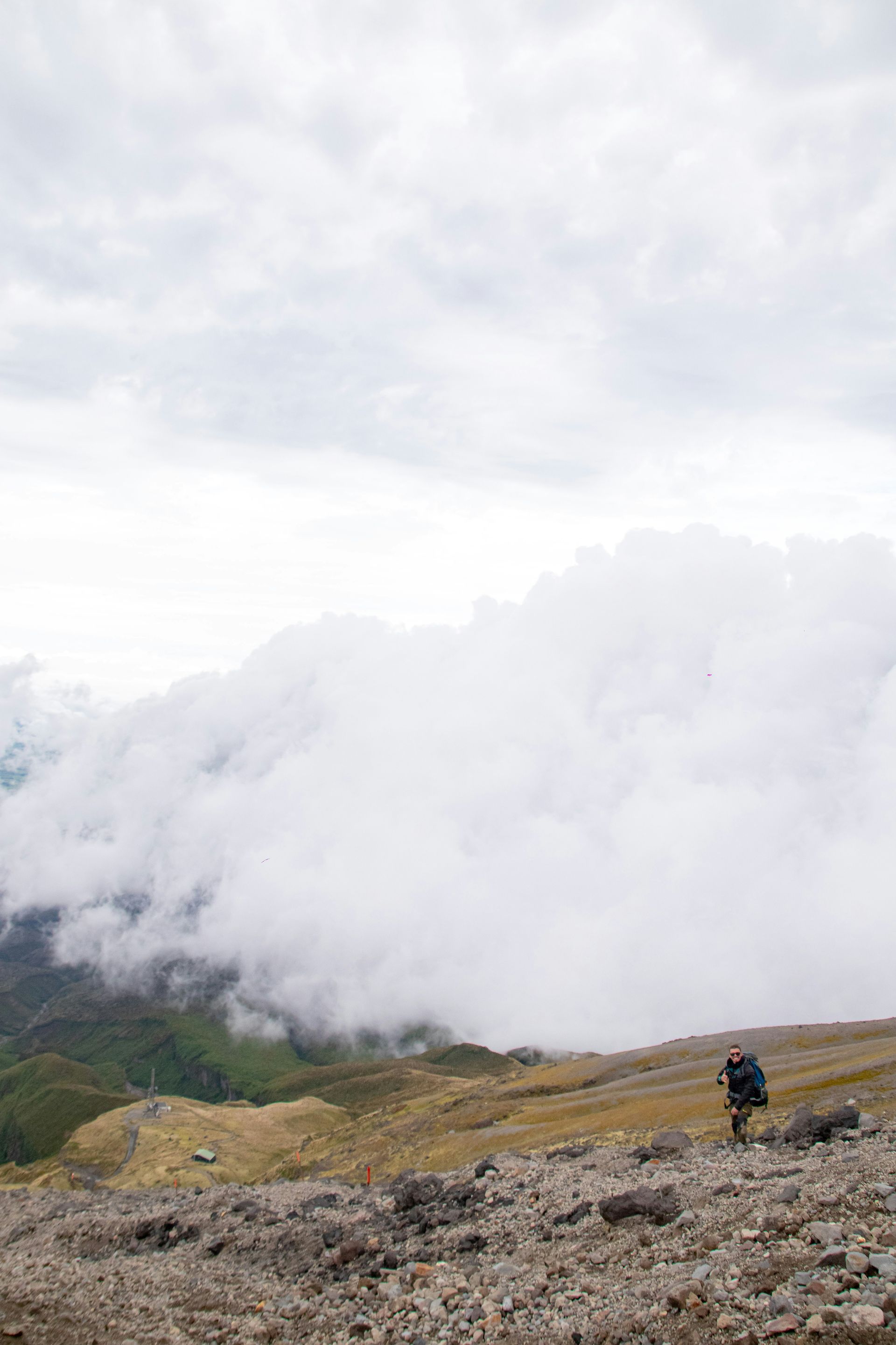 A person is hiking up the Mount Taranaki Summit Track, Taranaki, New Zealand, with clouds in the backround.