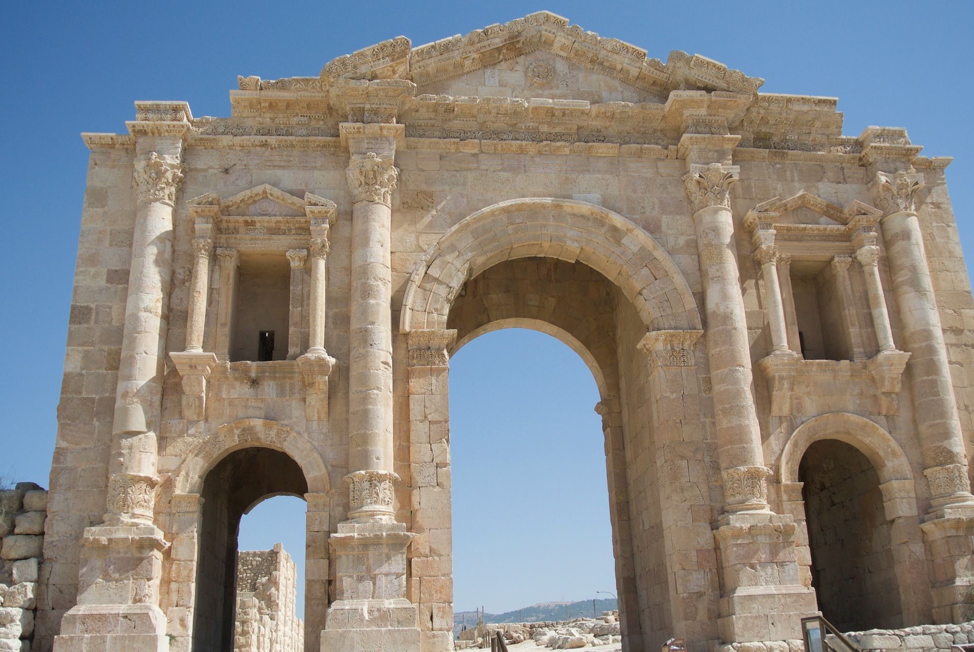 Arch of Triumph, Jerash, Jordan. Ancient Roman architecture, arched gateway with columns, sandstone color against blue sky.