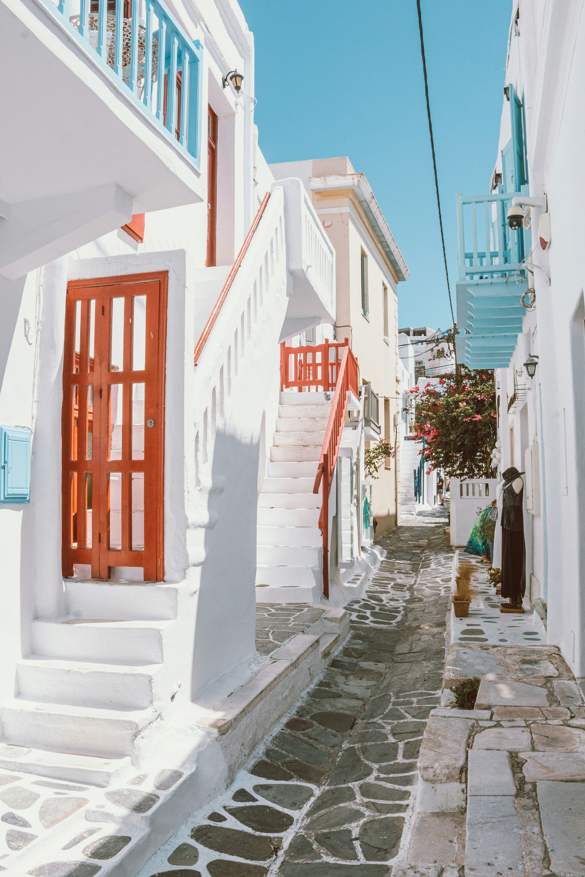 A narrow alleyway between two white buildings with stairs and a red door in Mykonos, Greece.
