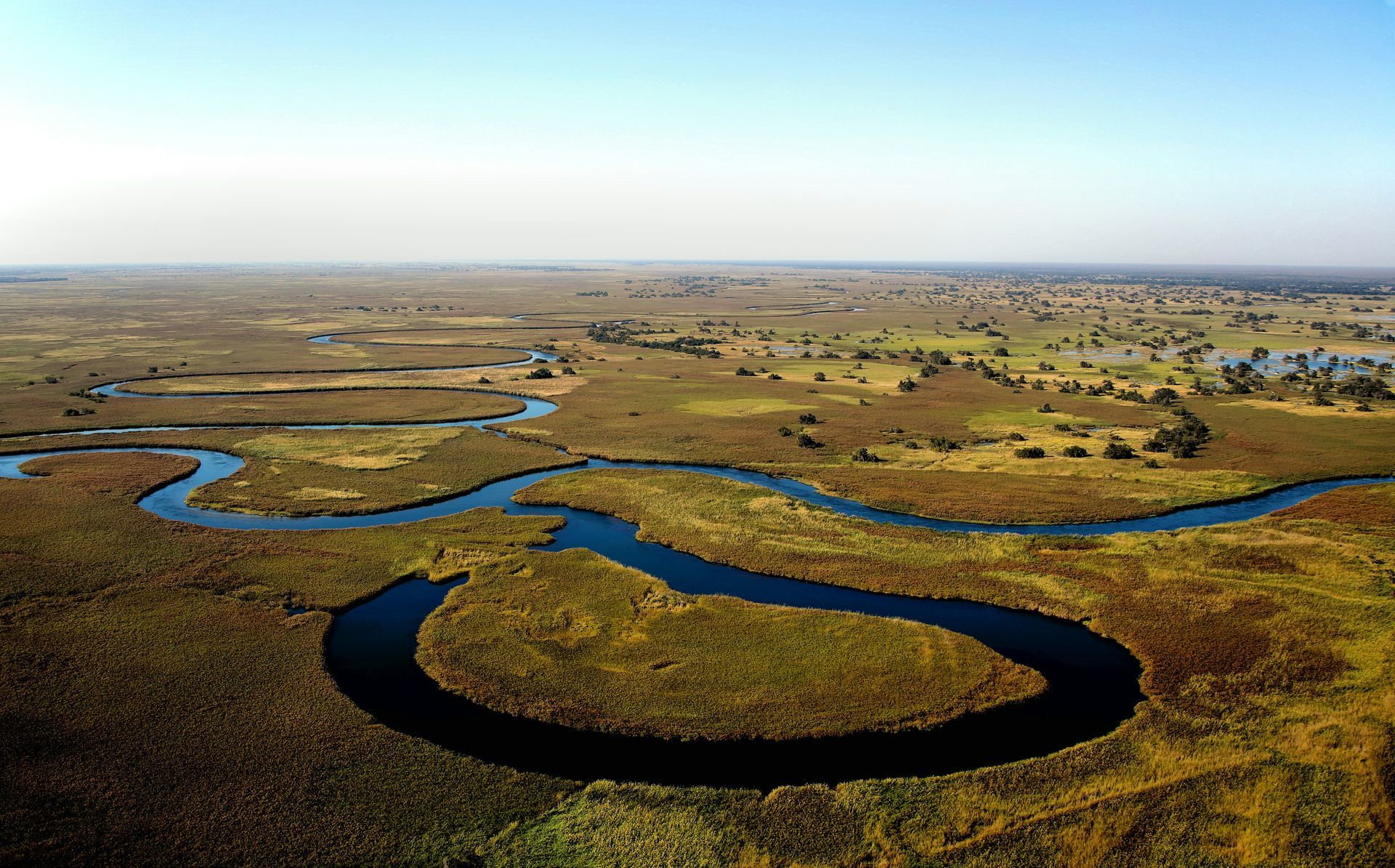 Aerial view of a winding river through a vast, grassy wetland at the Okavango Delta, Botswana.