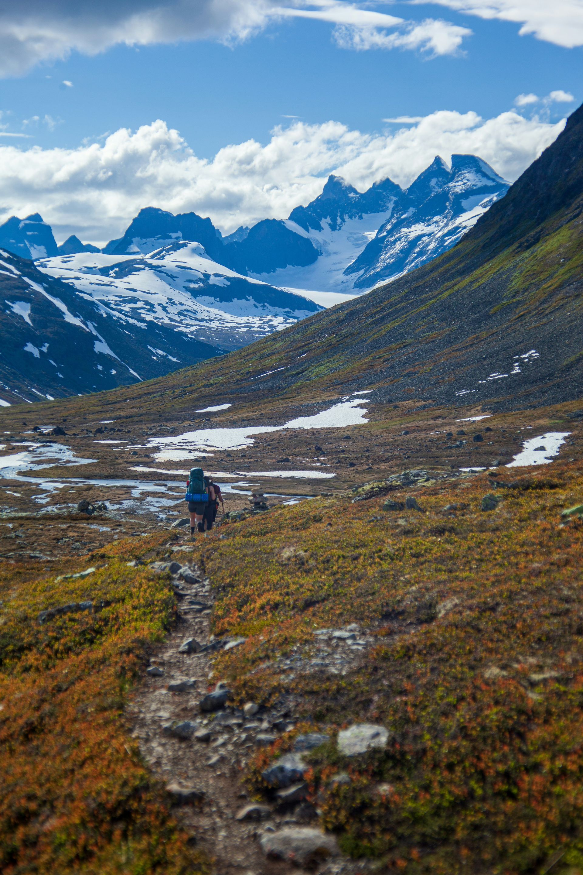 Hiker on trail in valley with snow-capped mountains in Jotunheimen National Park, Norway.