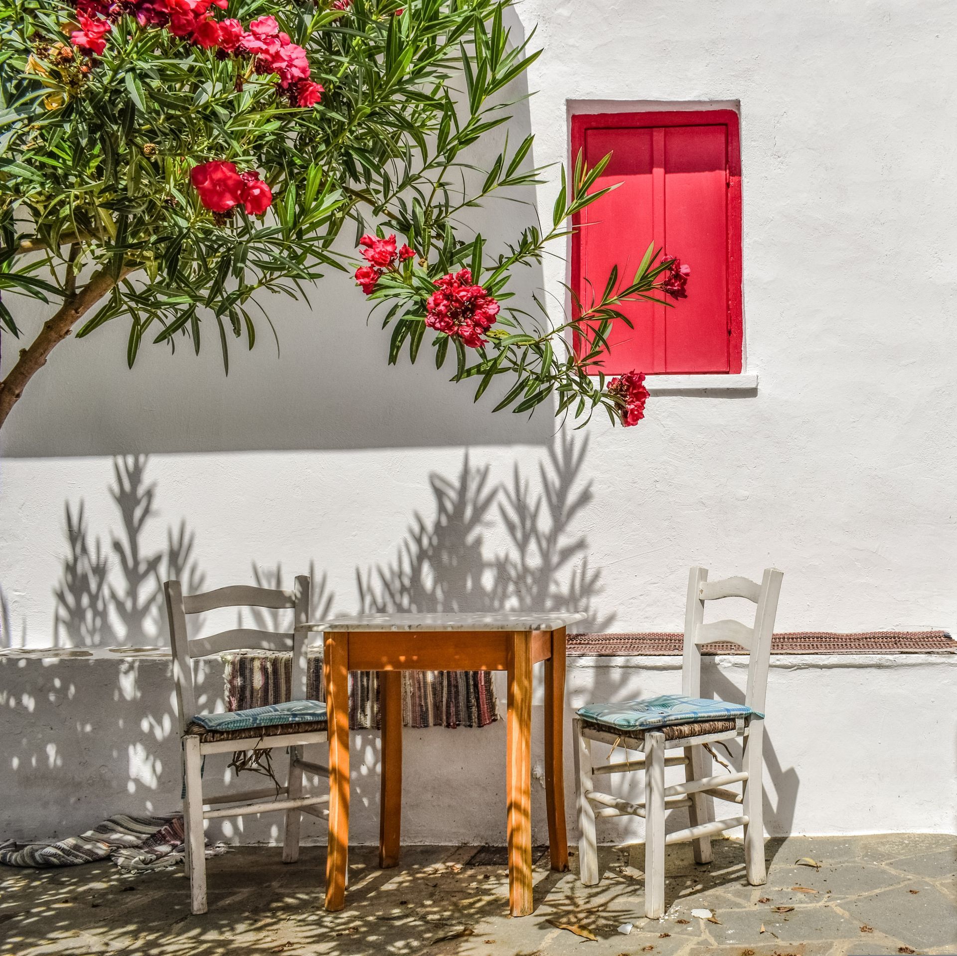 A table and chairs in front of a white building with pink shutters in Skopelos, Greece.
