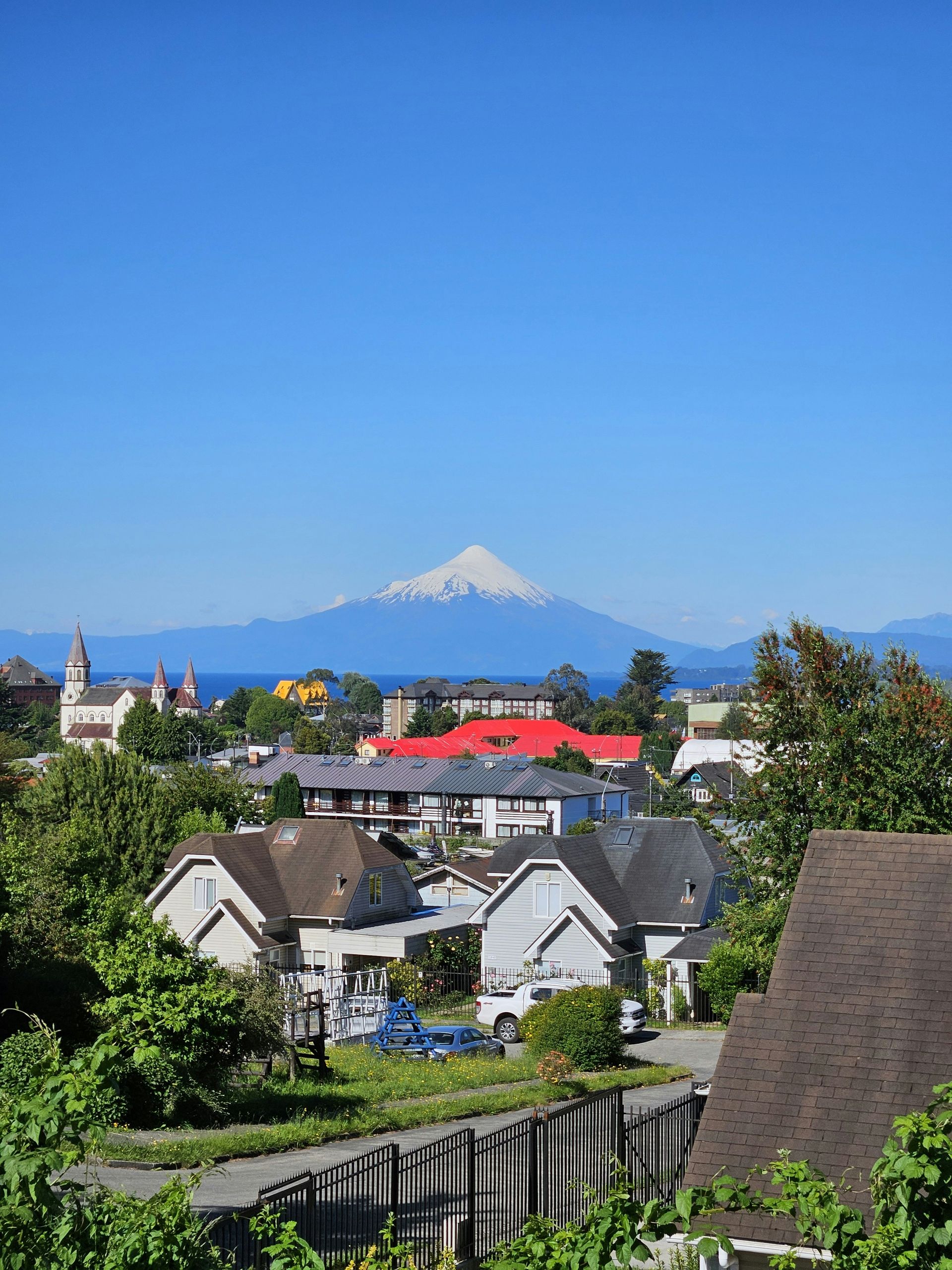 Houses and buildings nestled in a town, with a snow-capped volcano and blue sky in the distance in Punta Arenas, Chile.