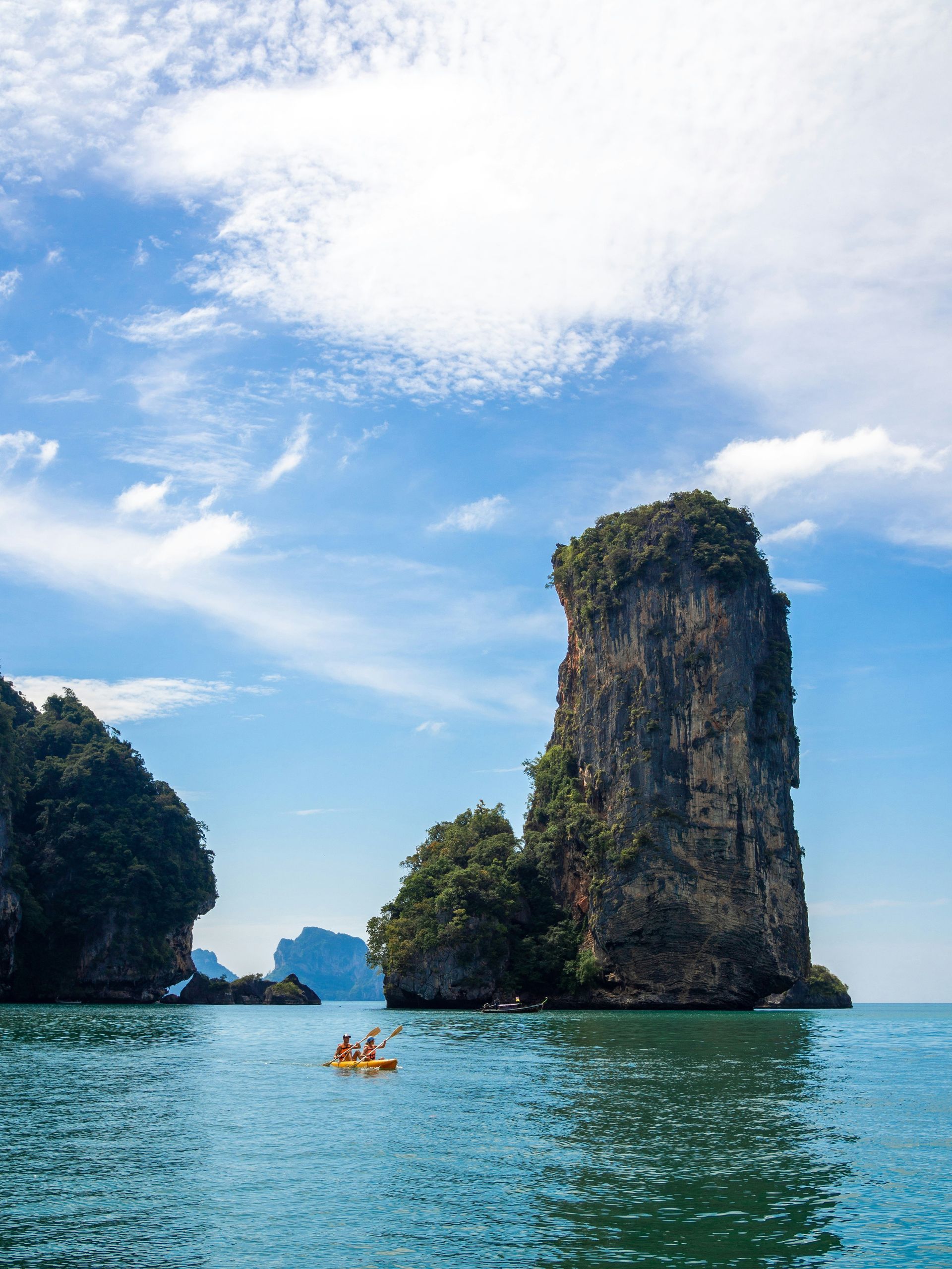 A couple of people are kayaking in the ocean near a large rock.